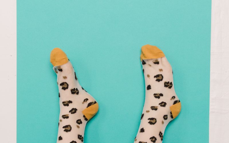 A person’s legs in sheer socks with a yellow leopard print pattern are raised against a turquoise background, styled and captured by Seattles best commercial food lifestyle photographer, with pink tape securing the paper to a white wall. captured by seattle food and lifestyle photographer Brooke Fitts