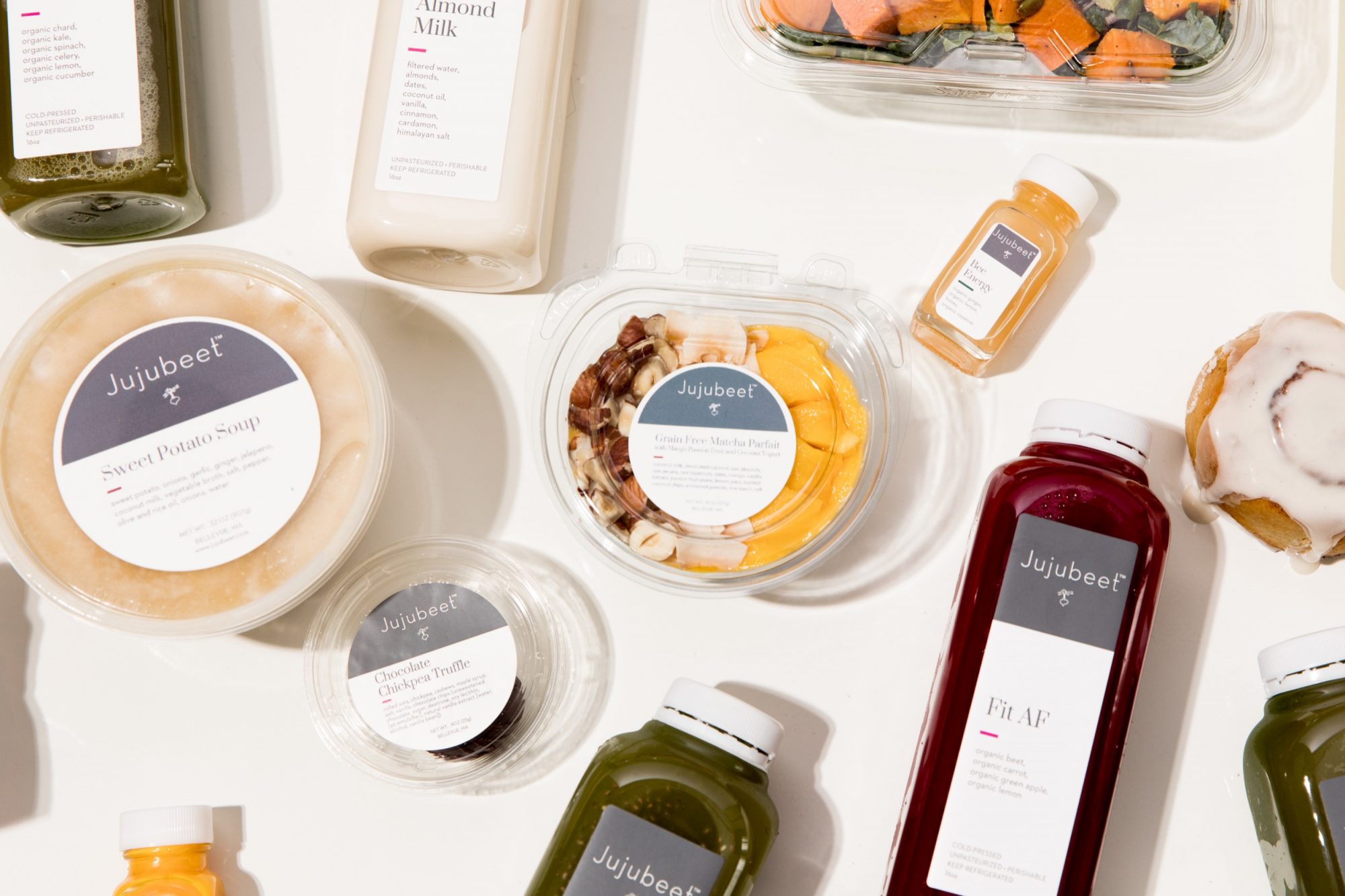 Seattle's best commercial food and hospitality photographer A variety of Jujubeet-branded healthy food and drink items, captured by Seattles best commercial food lifestyle photographer, are arranged on a white surface—including juices, soups, salads, almond milk, and a cinnamon roll. captured by seattle's best food and lifestyle photographer Brooke Fitts