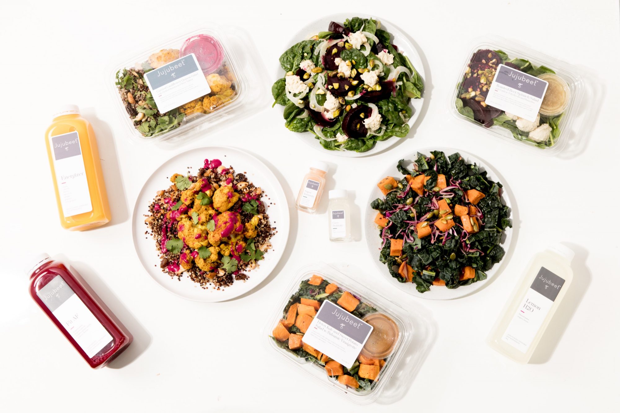 Seattle's best commercial food and hospitality photographer A variety of healthy meals, salads, and juices are arranged on a white surface in a vibrant scene by Seattles best commercial food lifestyle photographer, featuring leafy greens, roasted vegetables, labeled containers, and bottled drinks. captured by seattle's best food and lifestyle photographer Brooke Fitts