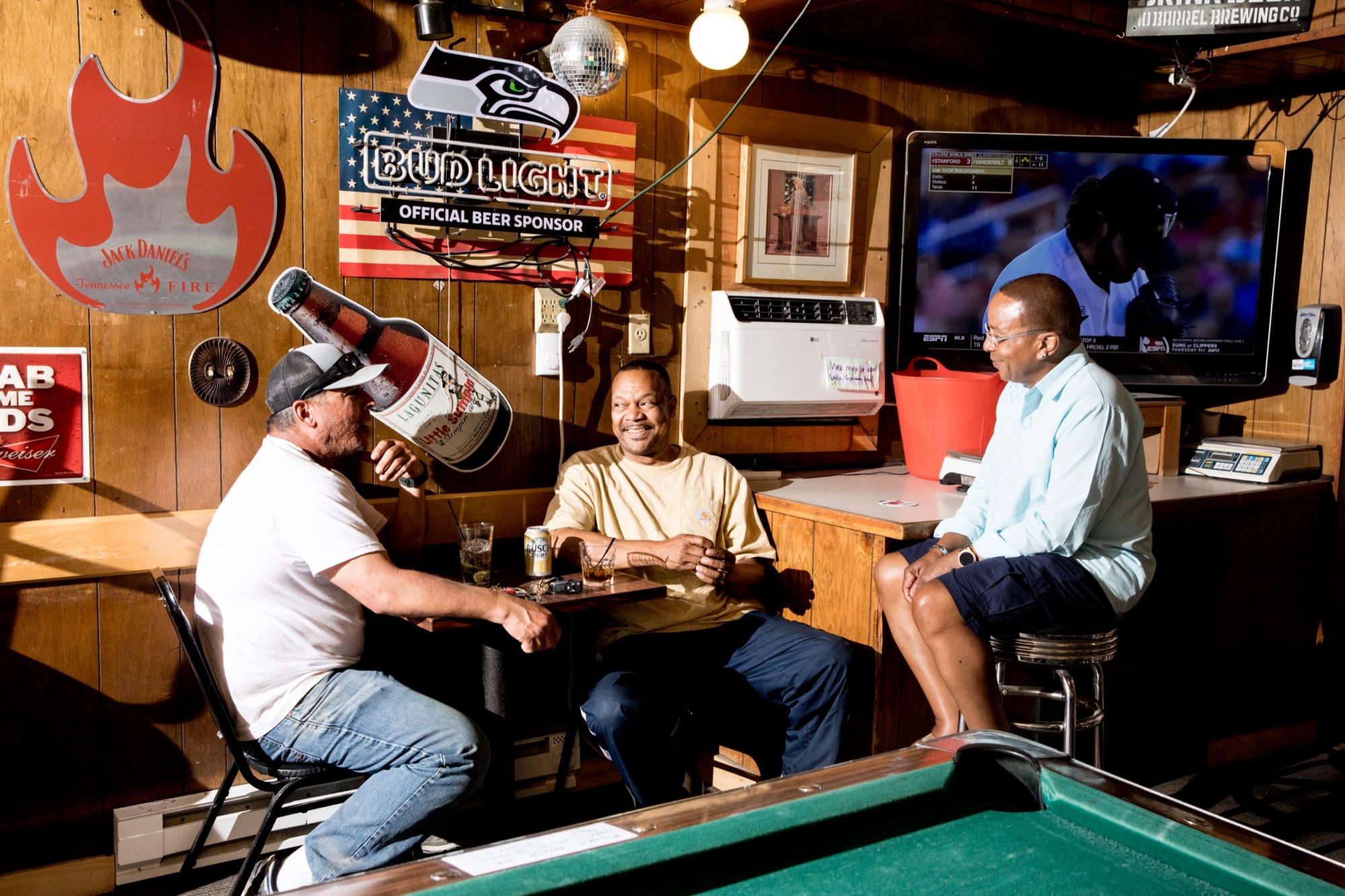 Seattle's best commercial food and hospitality photographer Three men sit and chat in a cozy, wood-paneled bar decorated with beer signs and sports memorabilia—an inviting scene captured by Seattles best commercial food lifestyle photographer. A TV shows baseball, with a pool table in the foreground. captured by seattle's best food and lifestyle photographer Brooke Fitts