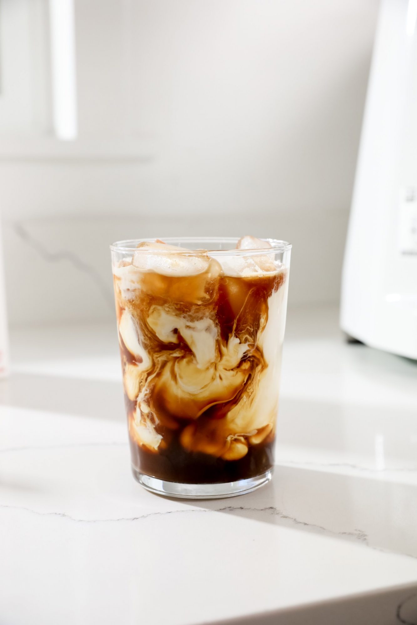 Seattle's best commercial food and hospitality photographer A glass of iced coffee with swirling cream sits on a white marble countertop, ice cubes visible and a bright, softly-lit background—captured by Seattles best commercial food lifestyle photographer. captured by seattle's best food and lifestyle photographer Brooke Fitts