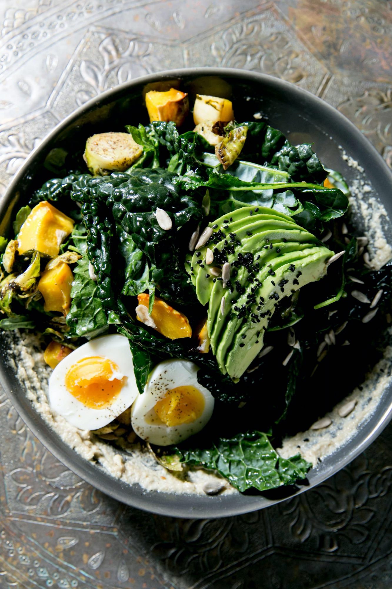 Seattle's best commercial food and hospitality photographer A bowl of salad with sliced avocado, soft-boiled eggs, roasted vegetables, kale, seeds, and creamy dressing, artfully captured by Seattles best commercial food lifestyle photographer on a decorative metal surface. captured by seattle's best food and lifestyle photographer Brooke Fitts