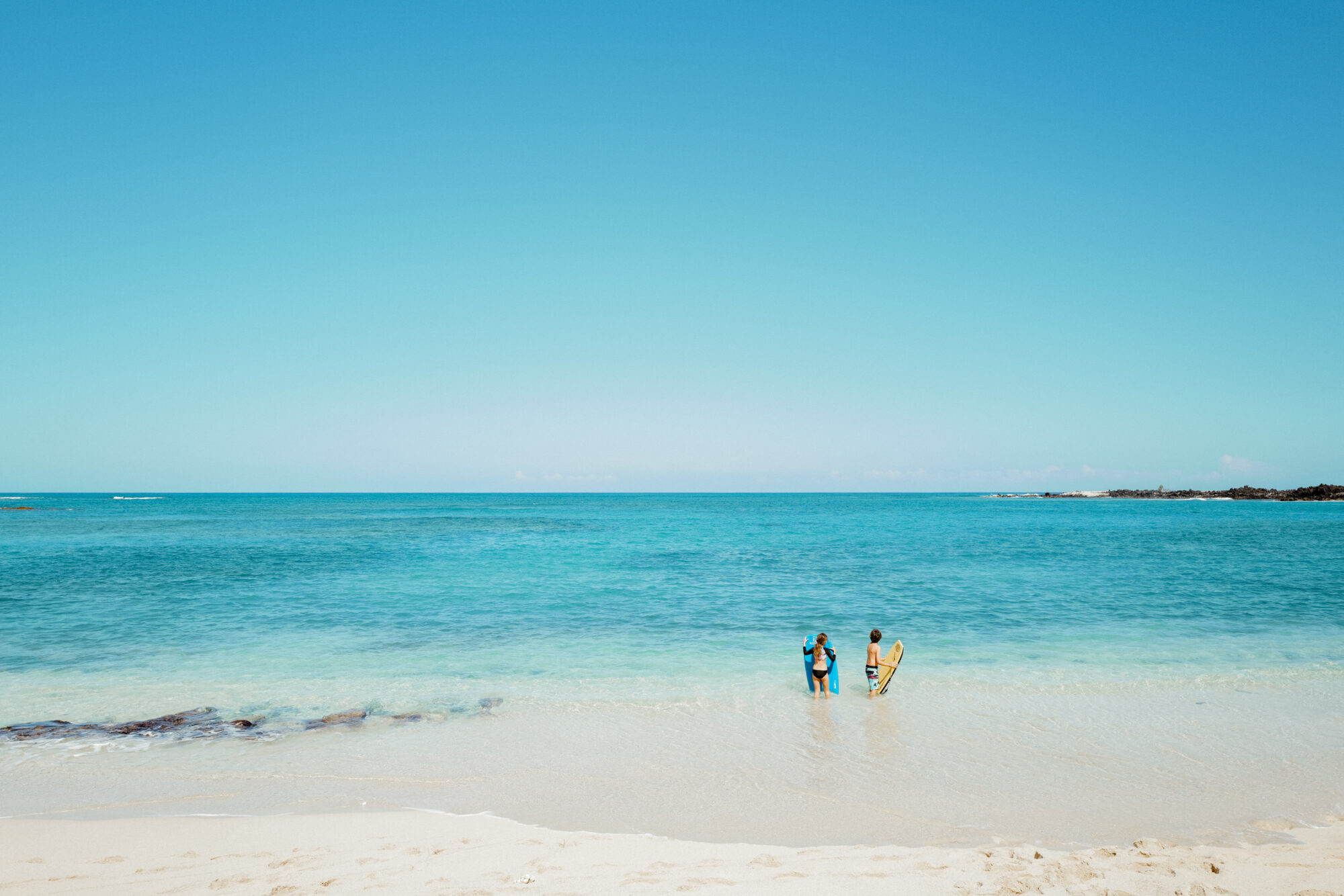 Seattle's best commercial food and hospitality photographer Two people stand in shallow, clear blue water near the shore of a sandy beach under a bright blue sky, with gentle waves and the horizon visible—captured by Seattles best commercial food lifestyle photographer. captured by seattle's best food and lifestyle photographer Brooke Fitts