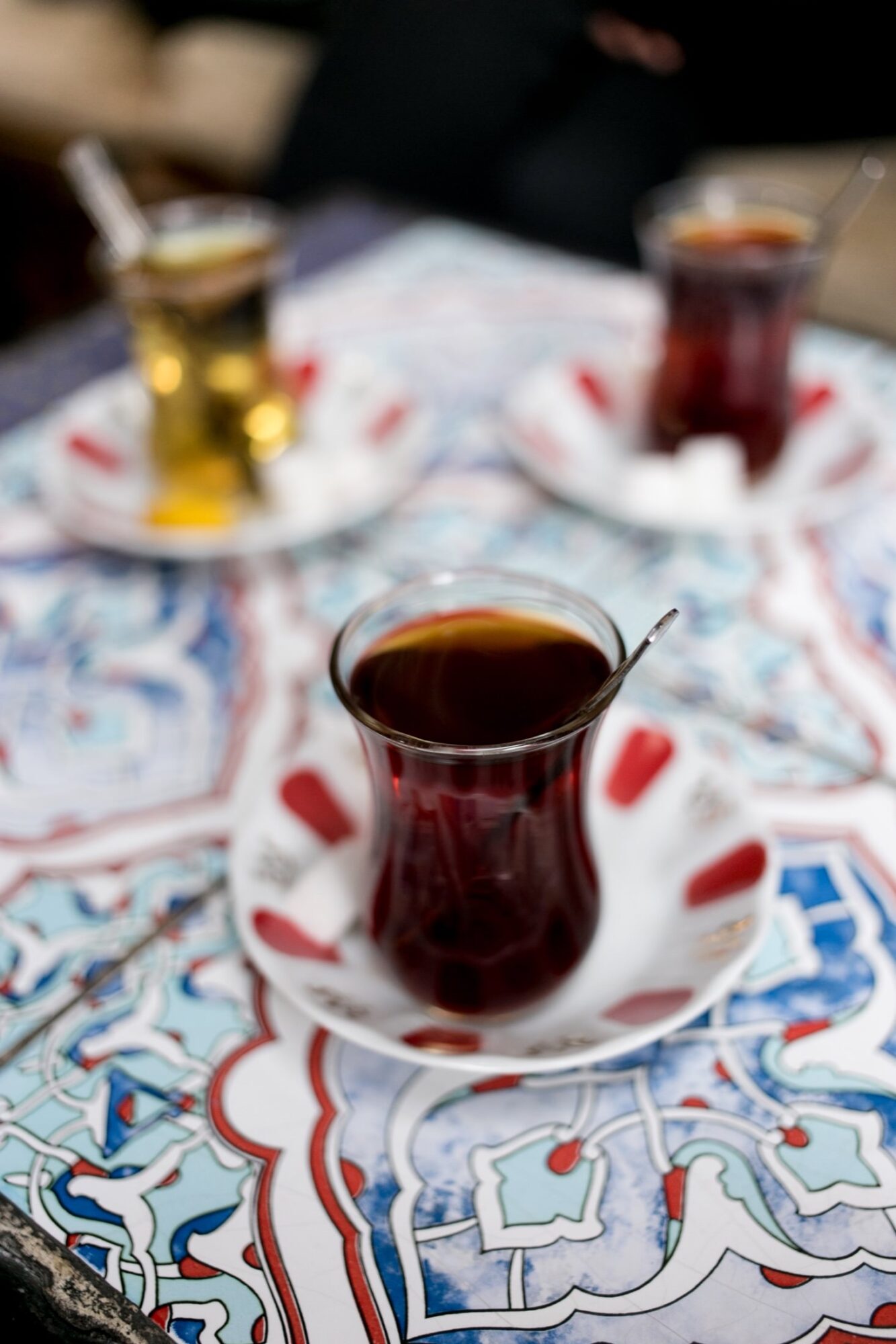 Seattle's best commercial food and hospitality photographer Three traditional Turkish tea glasses with spoons, two filled with dark tea and one with light tea, sit on patterned saucers atop a colorful, intricate tiled table—captured by Seattles best commercial food lifestyle photographer. captured by seattle's best food and lifestyle photographer Brooke Fitts