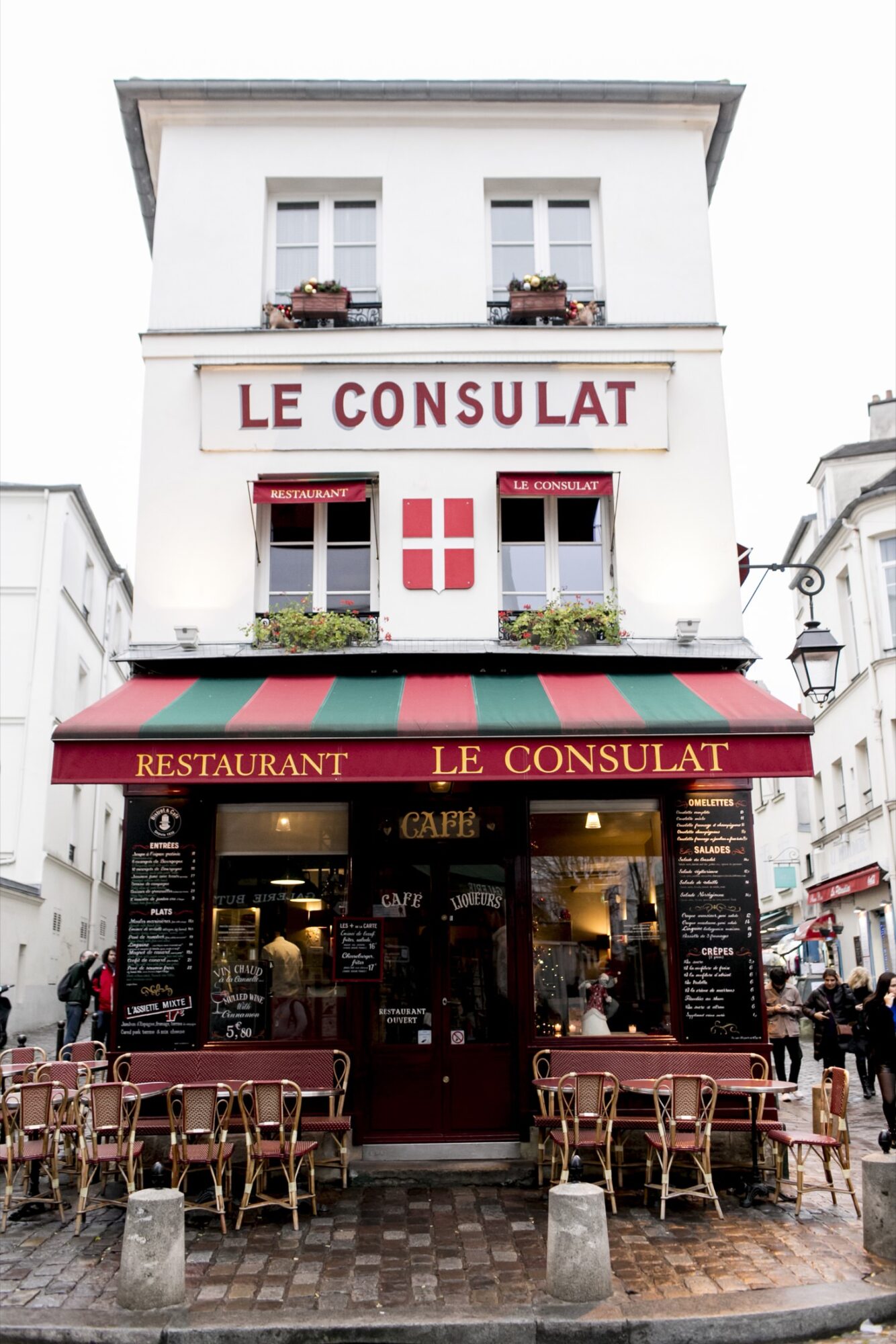 Seattle's best commercial food and hospitality photographer A classic Parisian café, Le Consulat, with a red and green awning, outdoor tables and chairs, and warm lights glowing inside on a cobblestone street—captured by Seattles best commercial food lifestyle photographer. captured by seattle's best food and lifestyle photographer Brooke Fitts