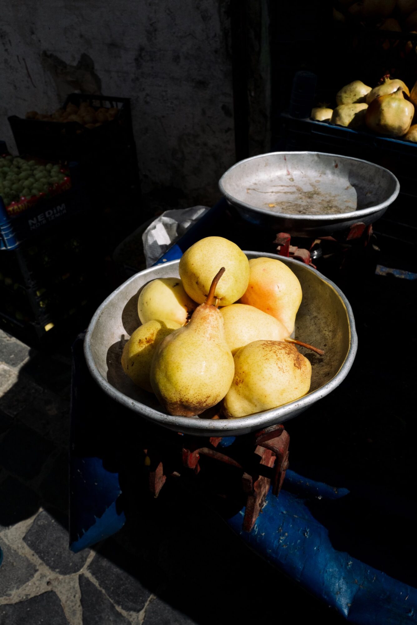 Seattle's best commercial food and hospitality photographer A metal scale holds several yellow pears with brown spots at an outdoor market, beautifully captured by Seattles best commercial food lifestyle photographer, with more fruit and crates in the background under natural sunlight. captured by seattle's best food and lifestyle photographer Brooke Fitts