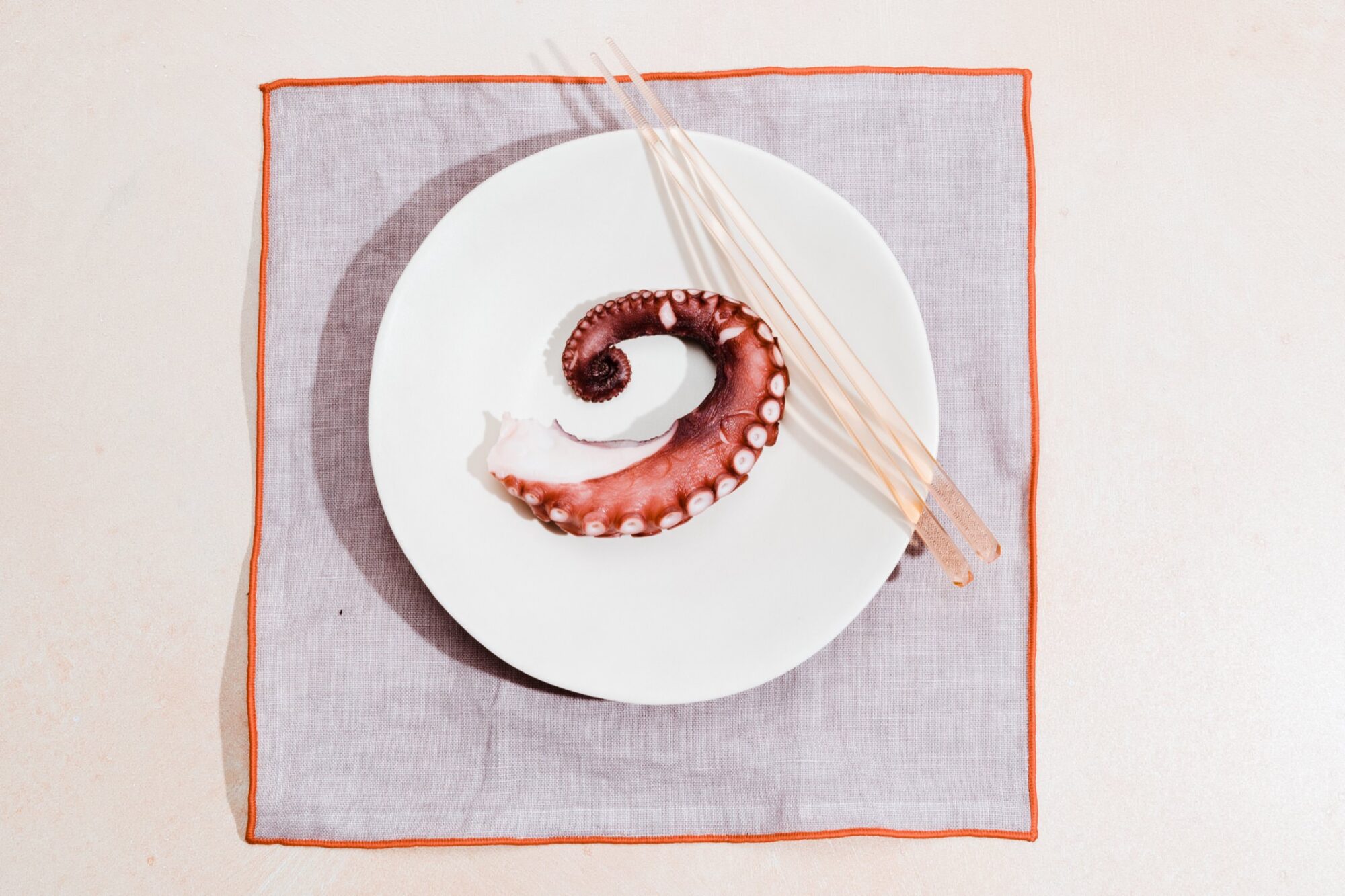 Seattle's best commercial food and hospitality photographer A single octopus tentacle on a white plate, placed on a gray napkin with orange trim. Three wooden chopsticks rest diagonally across the plate—captured by Seattles best commercial food lifestyle photographer. captured by seattle's best food and lifestyle photographer Brooke Fitts