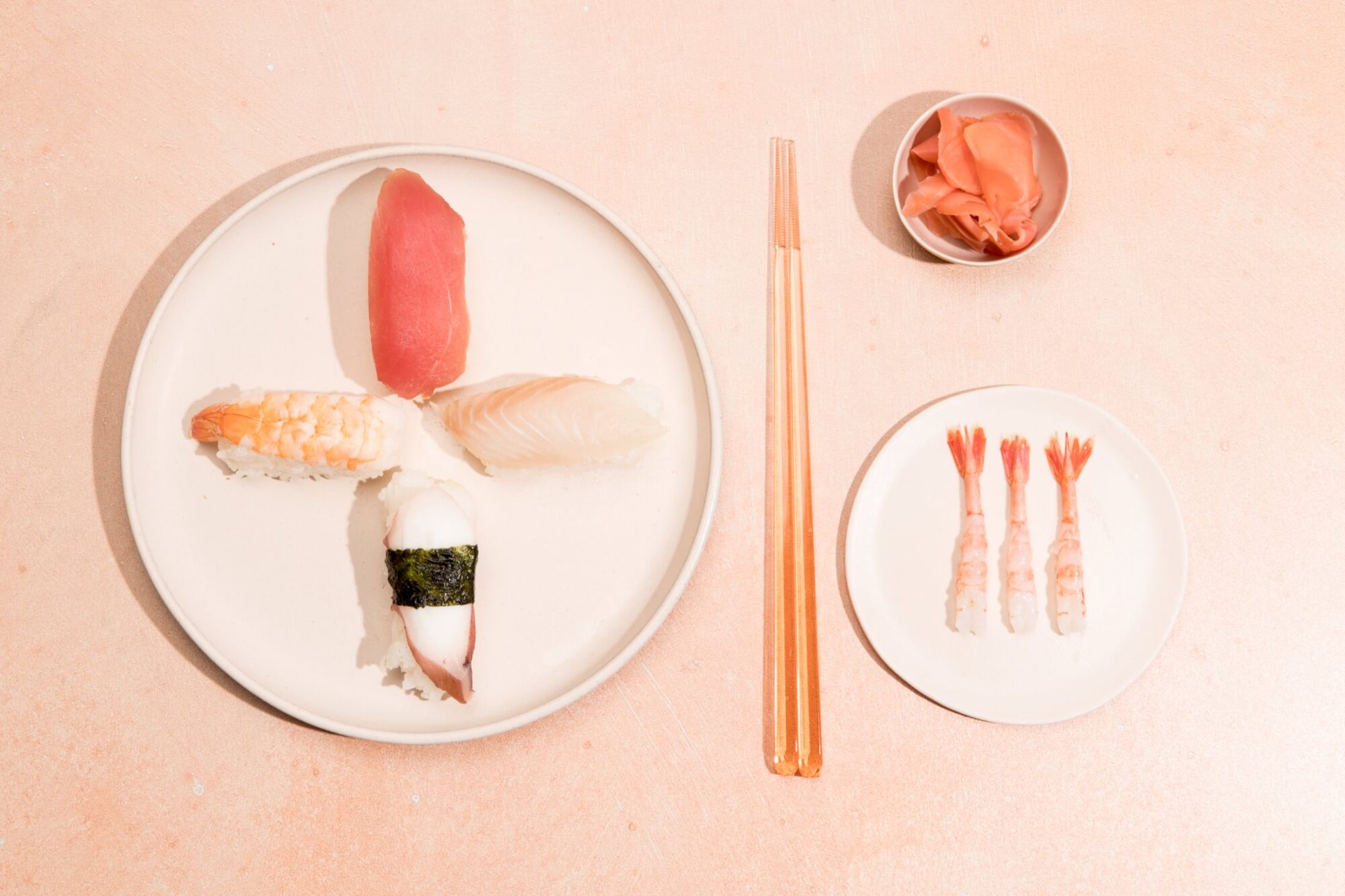 Seattle's best commercial food and hospitality photographer A plate with four pieces of sushi, a small dish of pickled ginger, orange chopsticks, and three peeled shrimp on a pale peach surface—captured by Seattles best commercial food lifestyle photographer. captured by seattle's best food and lifestyle photographer Brooke Fitts