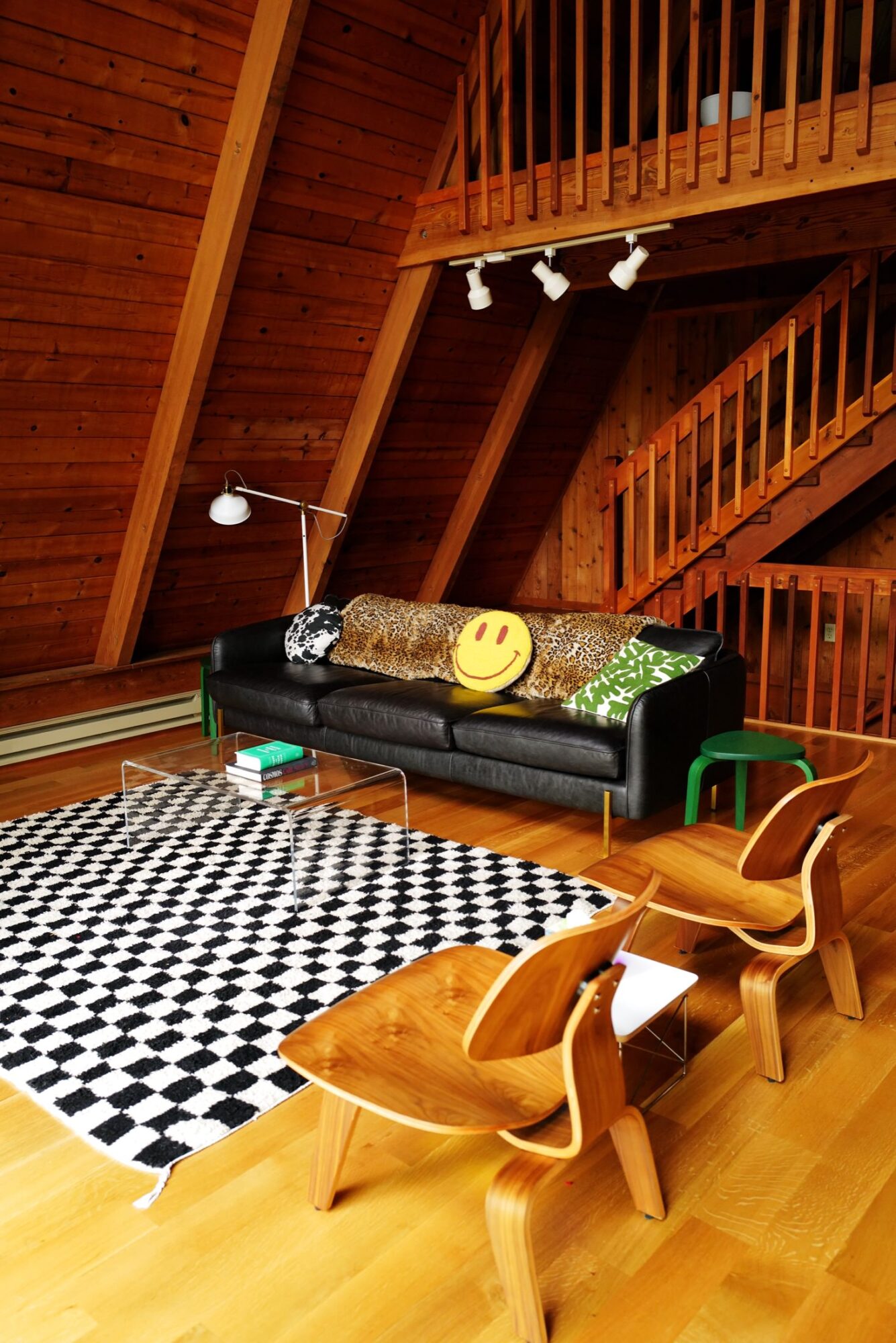 Seattle's best commercial food and hospitality photographer A cozy, modern A-frame cabin living room with wood-paneled walls, a black sofa with colorful pillows (including a smiley face), two wooden chairs, a checkered rug, and a loft—captured by Seattles best commercial food lifestyle photographer. captured by seattle's best food and lifestyle photographer Brooke Fitts