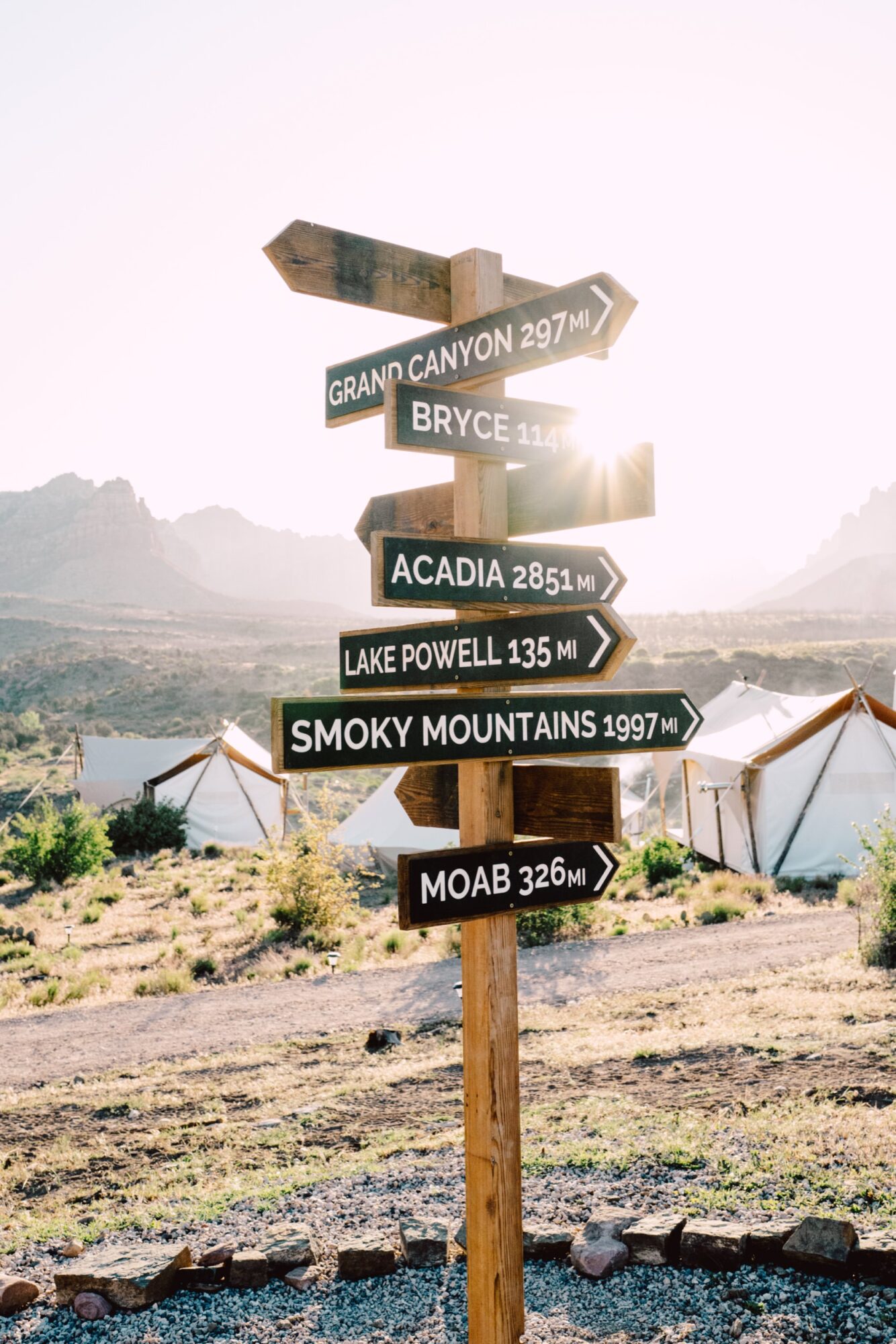 Seattle's best commercial food and hospitality photographer A wooden signpost with arrows points to destinations like Grand Canyon and Moab. White tents and mountains sit beneath bright sunlight—captured by Seattle’s best commercial food lifestyle photographer. captured by seattle's best food and lifestyle photographer Brooke Fitts
