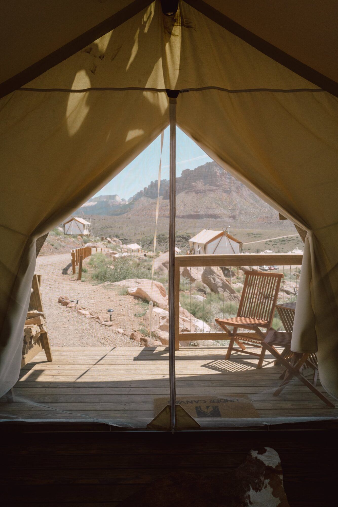 Seattle's best commercial food and hospitality photographer View from inside a tent captured by Seattles best commercial food lifestyle photographer, showing a wooden deck with two chairs overlooking a scenic, rocky landscape with mountains and other tents under a sunny sky. captured by seattle's best food and lifestyle photographer Brooke Fitts