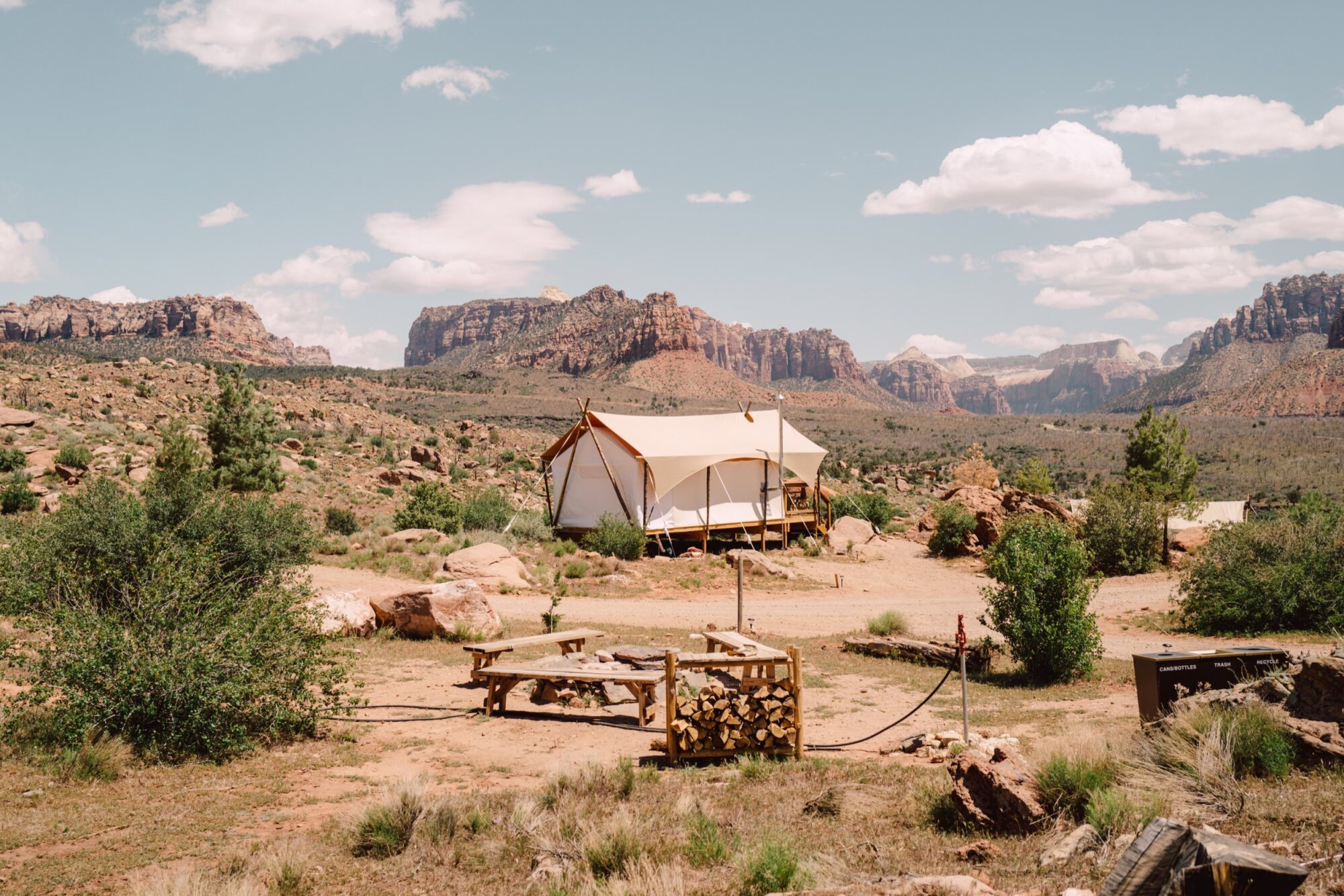 Seattle's best commercial food and hospitality photographer Canvas tent on a wooden platform in a desert landscape with rocky mountains, sparse vegetation, picnic table, and firewood—captured in the style of Seattles best commercial food lifestyle photographer beneath a clear blue sky. captured by seattle's best food and lifestyle photographer Brooke Fitts