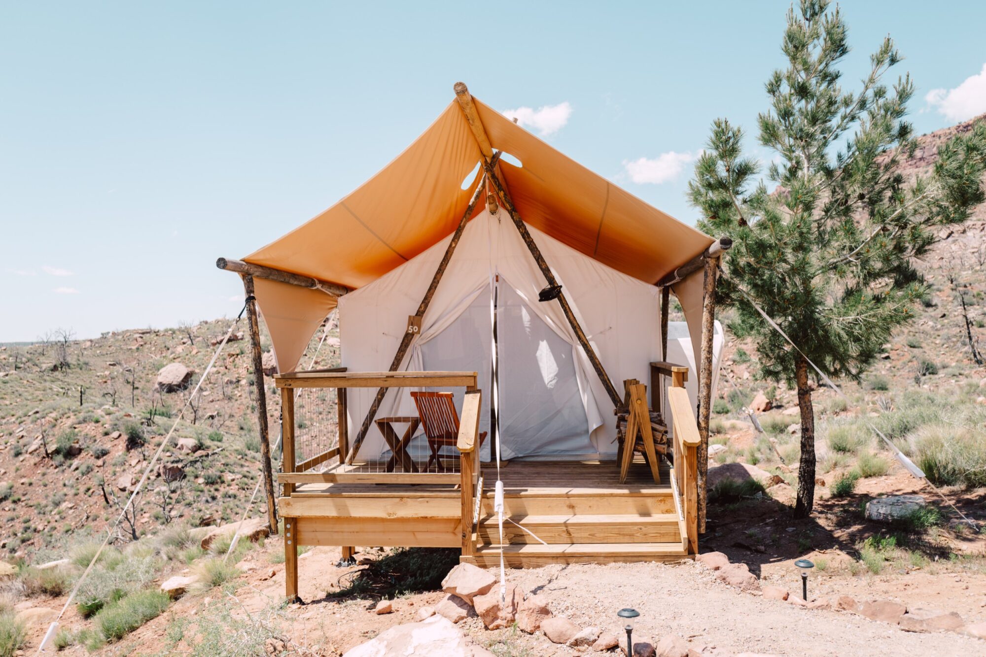 Seattle's best commercial food and hospitality photographer A canvas glamping tent with a wooden deck and two chairs is set up in a rocky, semi-arid landscape under a clear blue sky, captured in the signature style of Seattles best commercial food lifestyle photographer. captured by seattle's best food and lifestyle photographer Brooke Fitts