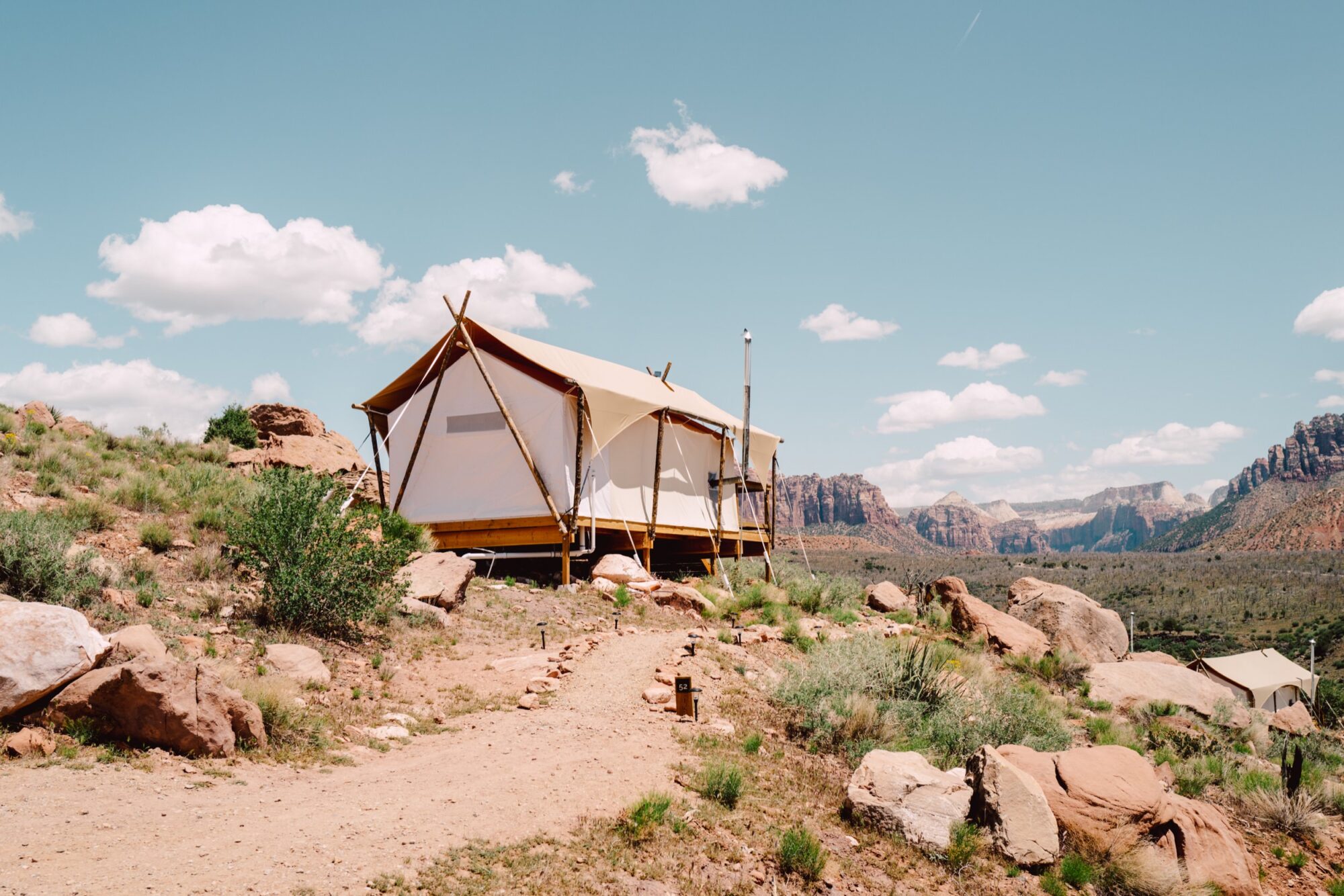 Seattle's best commercial food and hospitality photographer A canvas glamping tent sits on a rocky hillside under a blue sky with scattered clouds, captured by Seattles best commercial food lifestyle photographer, surrounded by desert vegetation and distant red rock mountains. captured by seattle's best food and lifestyle photographer Brooke Fitts