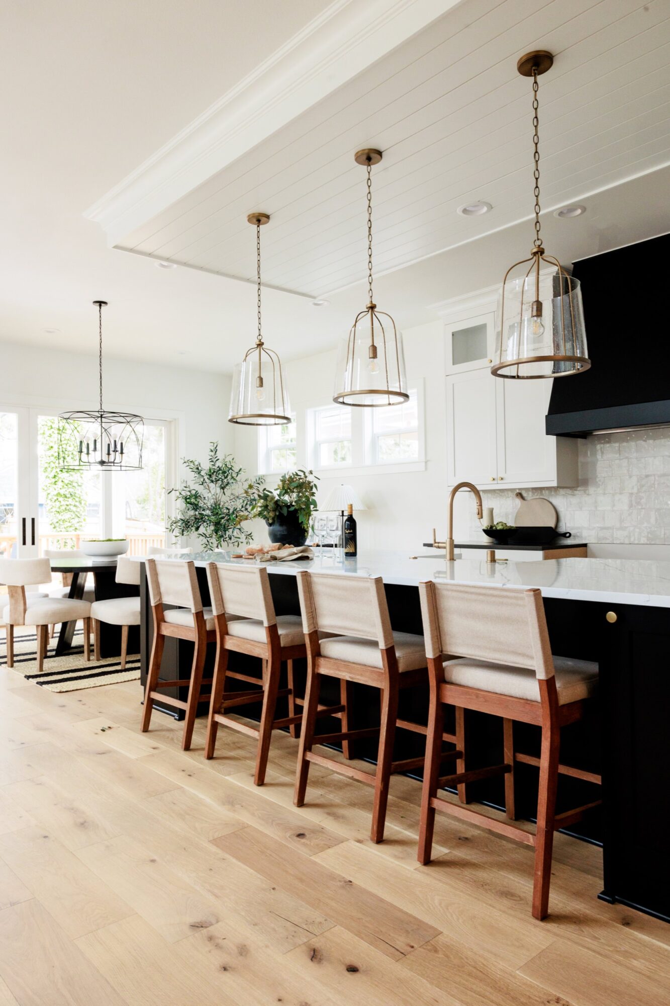 Seattle's best commercial food and hospitality photographer Modern kitchen with light wood floors, a long island with four cushioned barstools, gold pendant lights, white countertops, black cabinetry, and large windows letting in natural light—captured by Seattles best commercial food lifestyle photographer. captured by seattle's best food and lifestyle photographer Brooke Fitts