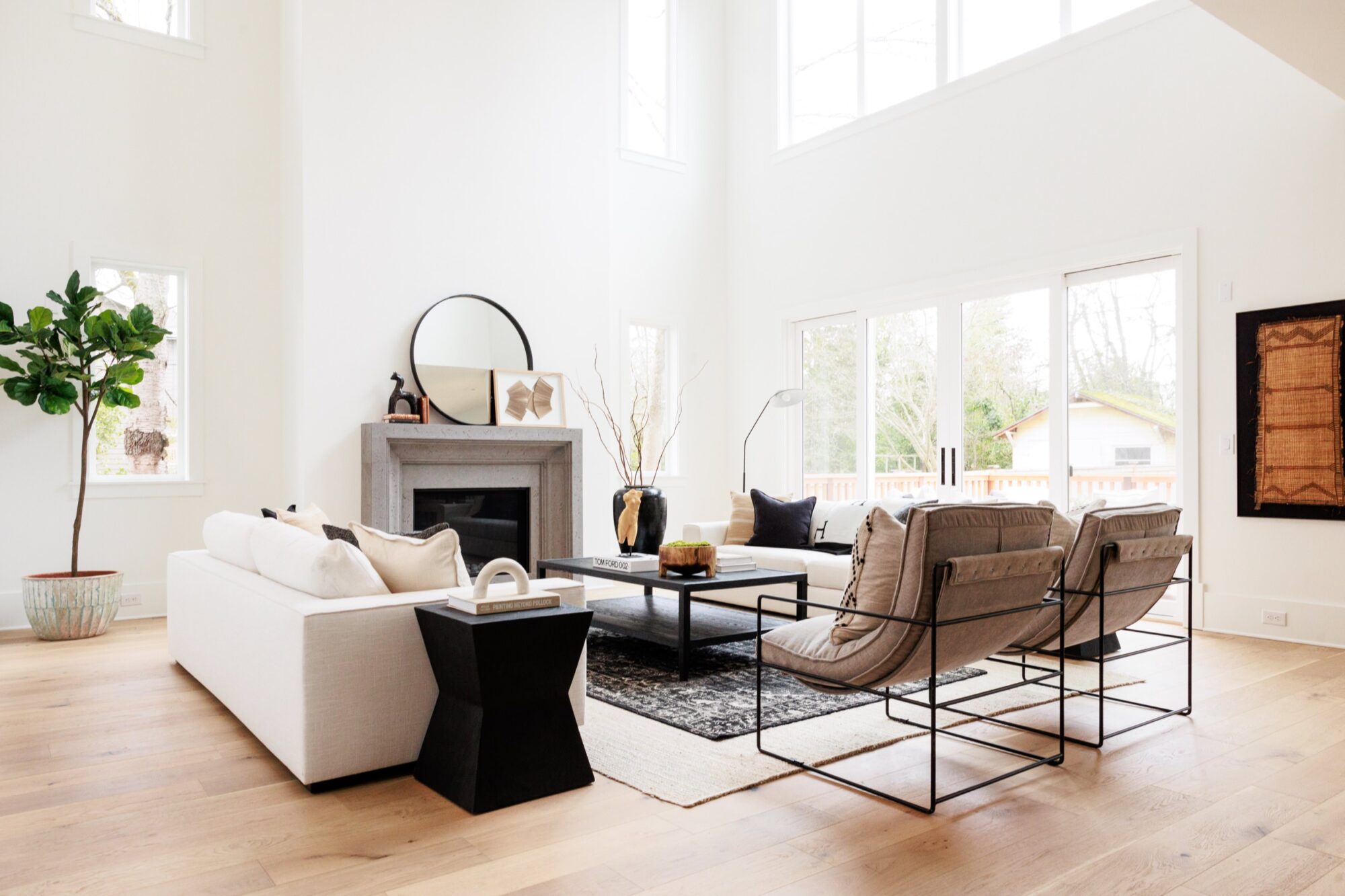 Seattle's best commercial food and hospitality photographer Bright, modern living room with large windows, a white sofa, two gray armchairs, and light wood flooring—styled like a scene from Seattles best commercial food lifestyle photographer. A black coffee table and fireplace with round mirror add inviting touches. captured by seattle's best food and lifestyle photographer Brooke Fitts