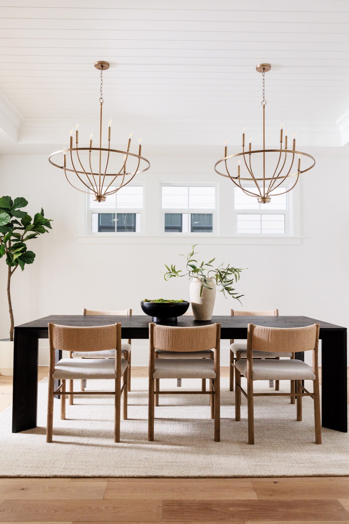 Seattle's best commercial food and hospitality photographer A modern dining room captured by Seattles best commercial food lifestyle photographer, featuring a black rectangular table, six wooden chairs with light cushions, globe chandeliers, vibrant plants, and three high windows on a white wall. captured by seattle's best food and lifestyle photographer Brooke Fitts