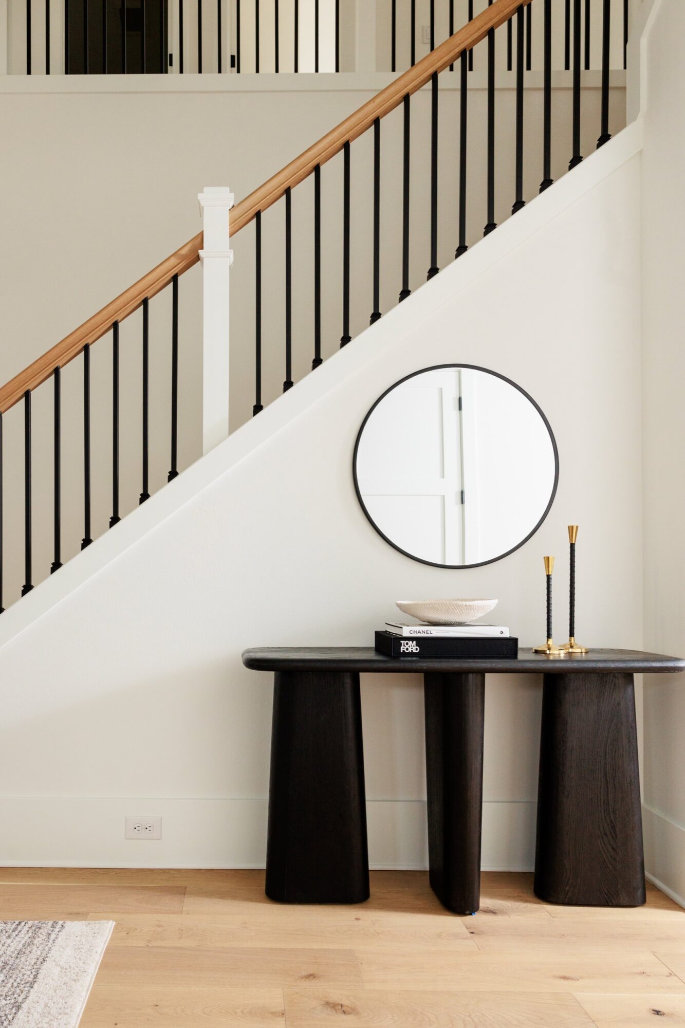 Seattle's best commercial food and hospitality photographer A modern entryway, captured by Seattles best commercial food lifestyle photographer, features a black console table with books, a bowl, and two candlesticks set against a white wall with a round mirror. A wooden staircase with black railings is in the background. captured by seattle's best food and lifestyle photographer Brooke Fitts