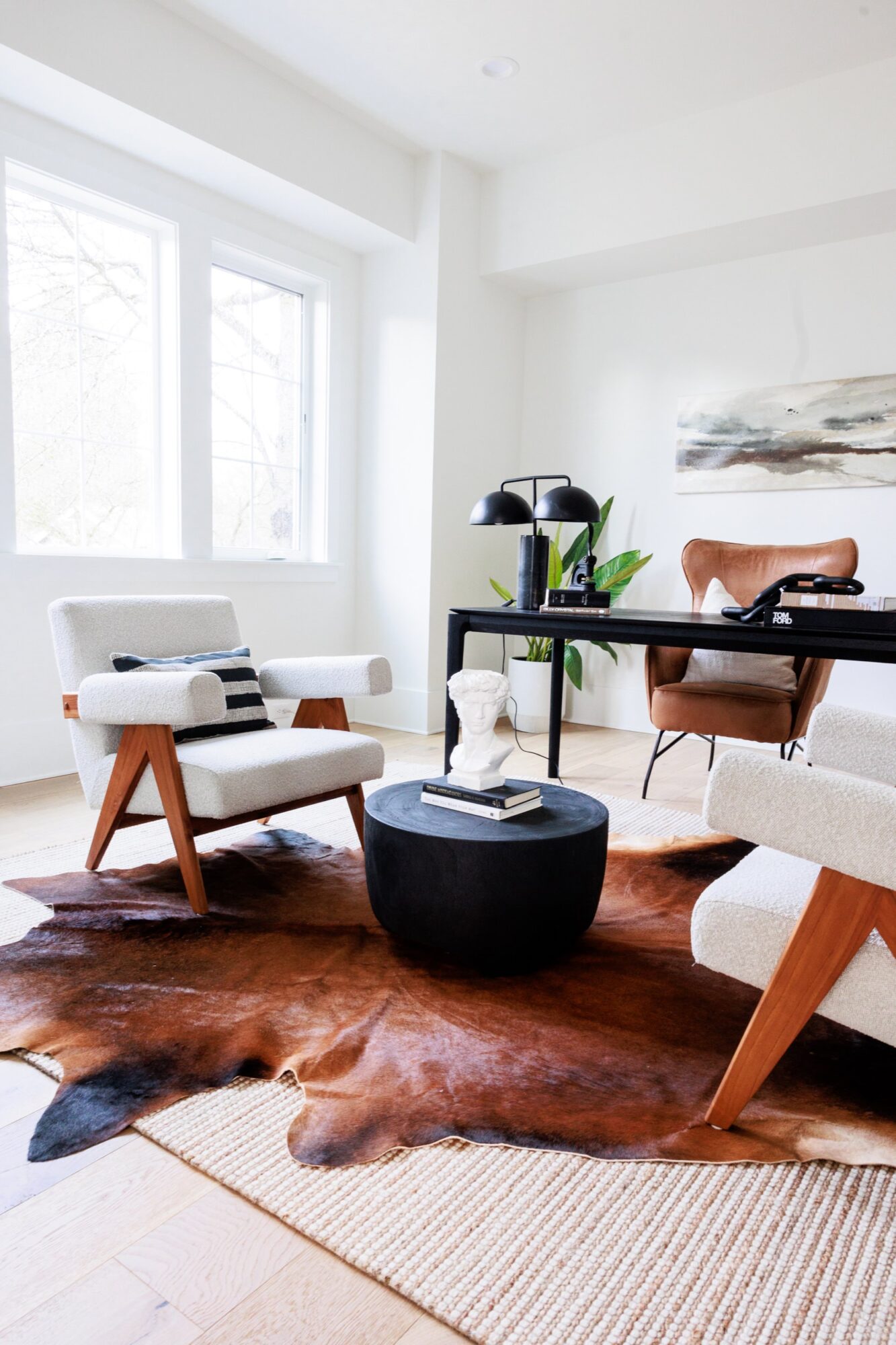 Seattle's best commercial food and hospitality photographer A modern home office, styled by Seattles best commercial food lifestyle photographer, features two white armchairs, a black round coffee table with a small statue, a brown leather desk chair, black desk, large windows, and layered rugs including a cowhide. captured by seattle's best food and lifestyle photographer Brooke Fitts