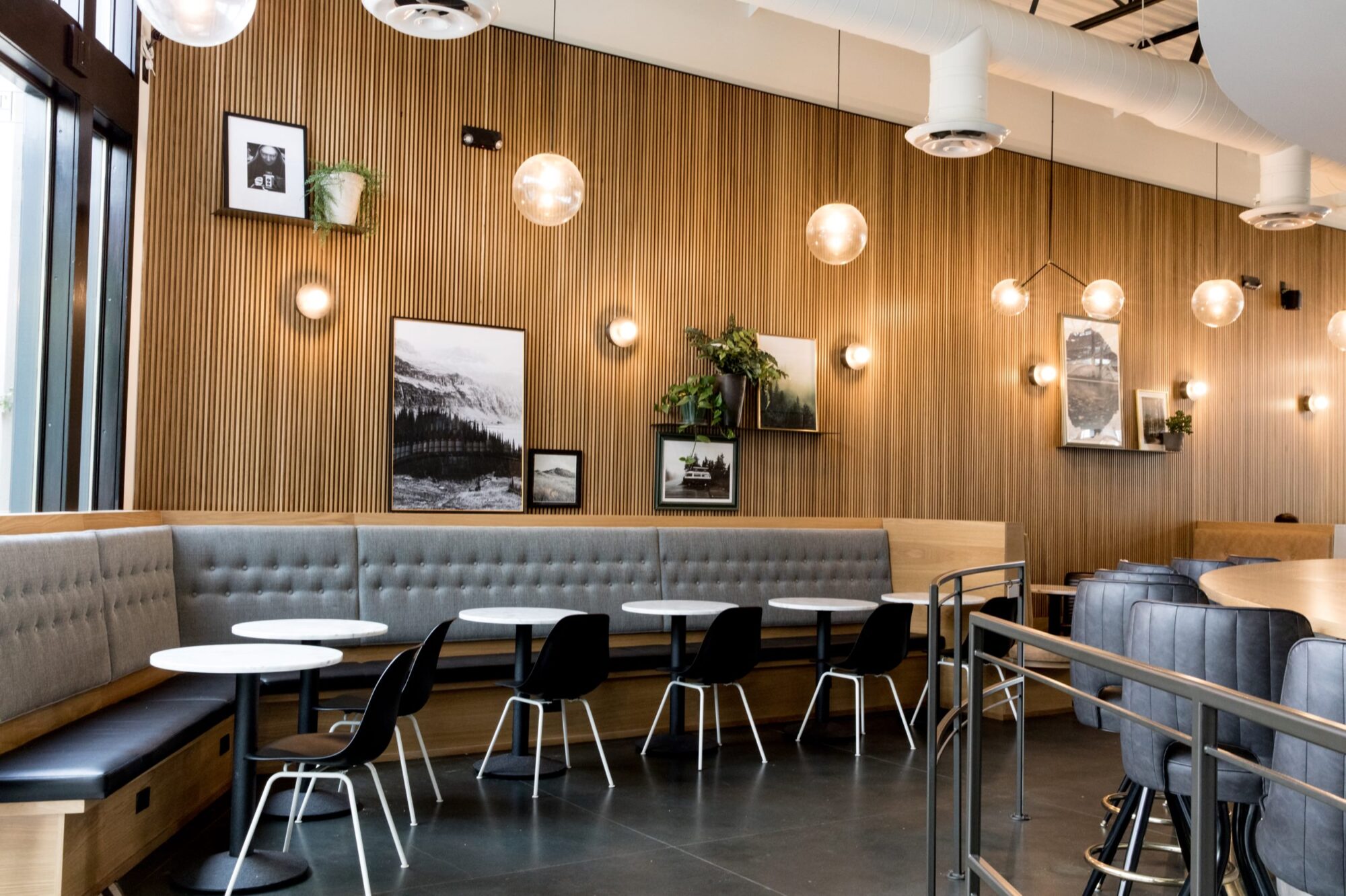 Seattle's best commercial food and hospitality photographer A modern cafe with wooden walls, round tables, black chairs, and gray cushioned bench seating is beautifully captured by Seattles best commercial food lifestyle photographer. Globe pendant lights and framed photos complete this well-lit, inviting space. captured by seattle's best food and lifestyle photographer Brooke Fitts