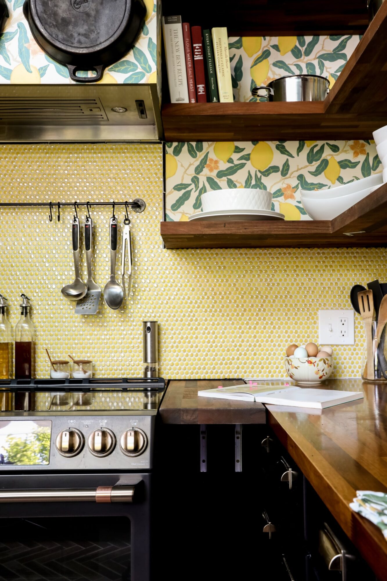 Seattle's best commercial food and hospitality photographer Modern kitchen corner with yellow honeycomb tile backsplash, lemon-patterned wallpaper, wooden shelves, and utensils above a stainless steel stove—captured by Seattles best commercial food lifestyle photographer. A teacup and eggs rest on the counter. captured by seattle's best food and lifestyle photographer Brooke Fitts