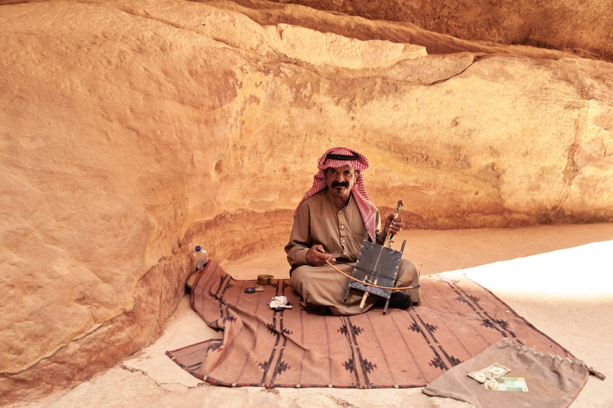 Seattle's best commercial food and hospitality photographer A man in traditional Middle Eastern clothing sits on a patterned rug against a sandstone wall, playing a stringed instrument as sunlight illuminates the scene—captured by Seattles best commercial food lifestyle photographer. captured by seattle's best food and lifestyle photographer Brooke Fitts