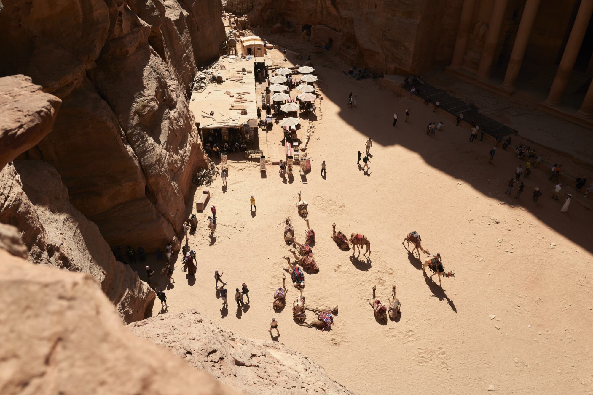 Seattle's best commercial food and hospitality photographer Aerial view of Petra’s ancient sandstone ruins in Jordan, with people walking, camels resting on the sandy ground, and a shaded market area—captured with the artistry of Seattles best commercial food lifestyle photographer. captured by seattle's best food and lifestyle photographer Brooke Fitts