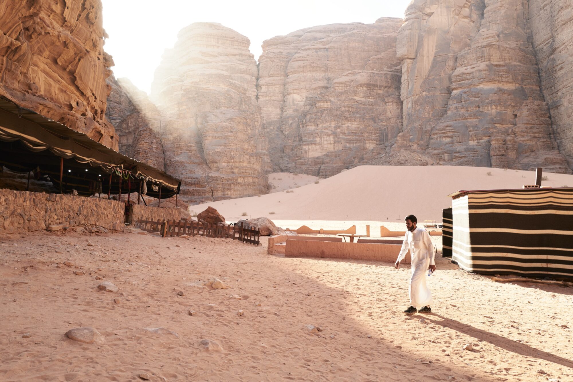 Seattle's best commercial food and hospitality photographer A man in traditional white clothing walks on sandy ground between tents in a desert canyon, sunlight streaming over towering rocky cliffs—captured through the lens of Seattles best commercial food lifestyle photographer. captured by seattle's best food and lifestyle photographer Brooke Fitts