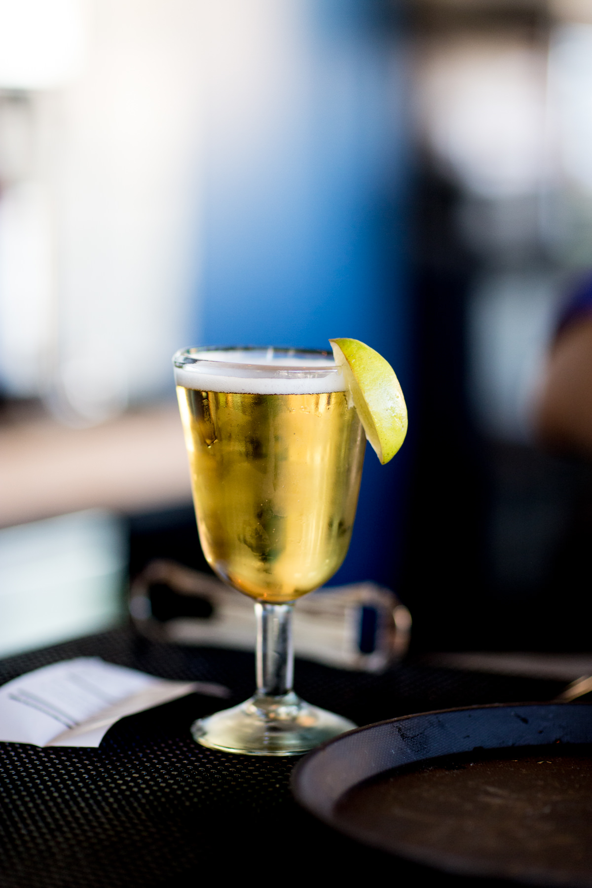 Seattle's best commercial food and hospitality photographer A glass of pale beer with a frothy head, garnished with a lemon wedge, sits on a dark surface beside a metal bottle opener and paper—captured by Seattles best commercial food lifestyle photographer. The background is softly blurred. captured by seattle's best food and lifestyle photographer Brooke Fitts