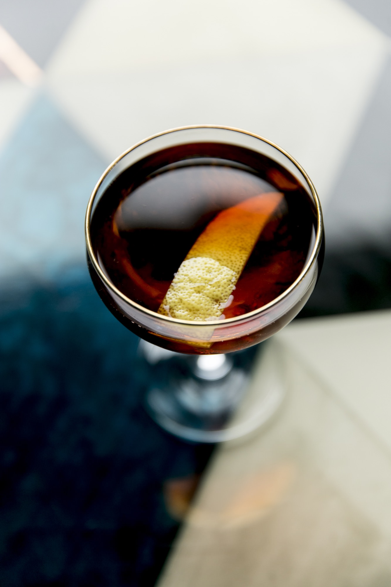 Seattle's best commercial food and hospitality photographer A close-up by Seattles best commercial food lifestyle photographer: a cocktail in a coupe glass, filled with dark liquid and garnished with lemon peel, set on a geometric patterned table. captured by seattle's best food and lifestyle photographer Brooke Fitts