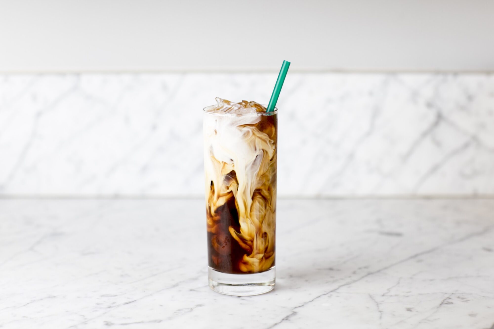 Seattle's best commercial food and hospitality photographer A tall glass of iced coffee with swirling cream, a green straw, and ice sits on a white marble countertop—captured by Seattles best commercial food lifestyle photographer. captured by seattle's best food and lifestyle photographer Brooke Fitts