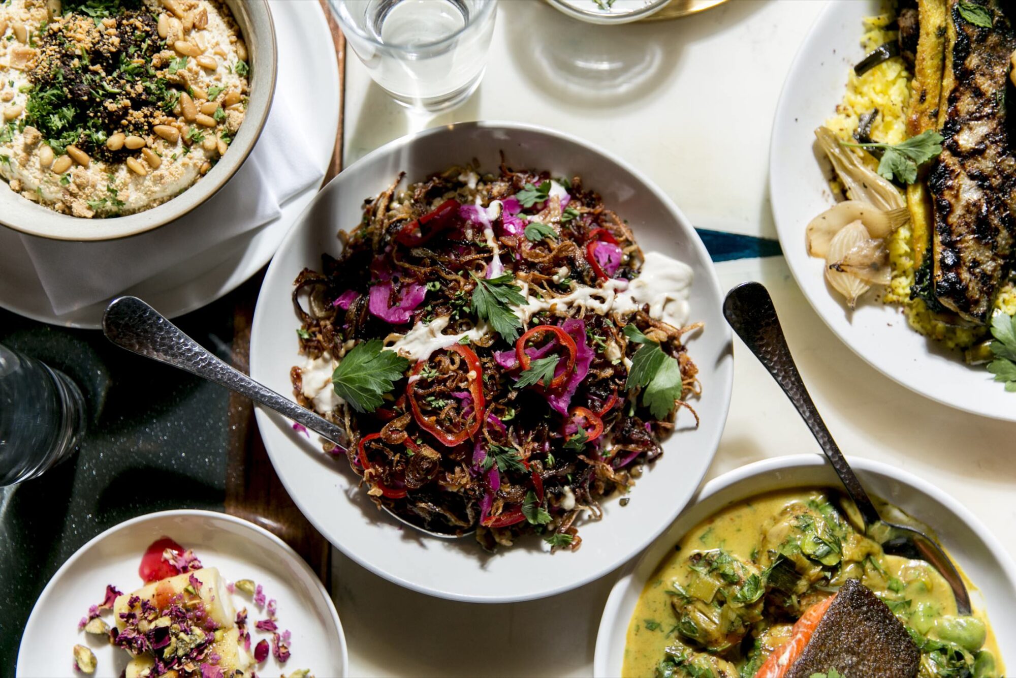 Seattle's best commercial food and hospitality photographer An overhead view by Seattles best commercial food lifestyle photographer features several dishes: a bowl of rice topped with herbs and nuts, grilled vegetables, a curry dish, and a large salad garnished with fresh herbs and red onions. captured by seattle's best food and lifestyle photographer Brooke Fitts