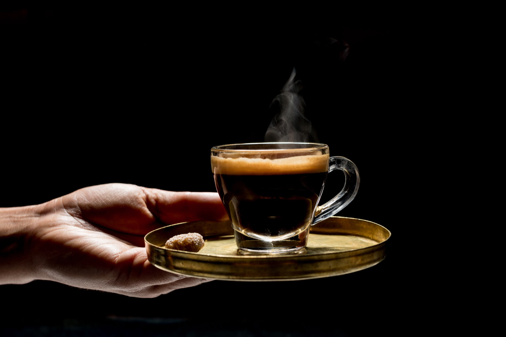 Seattle's best commercial food and hospitality photographer A hand holds a golden tray with a steaming cup of espresso and a single sugar cube against a dark background, captured by Seattles best commercial food lifestyle photographer. captured by seattle's best food and lifestyle photographer Brooke Fitts