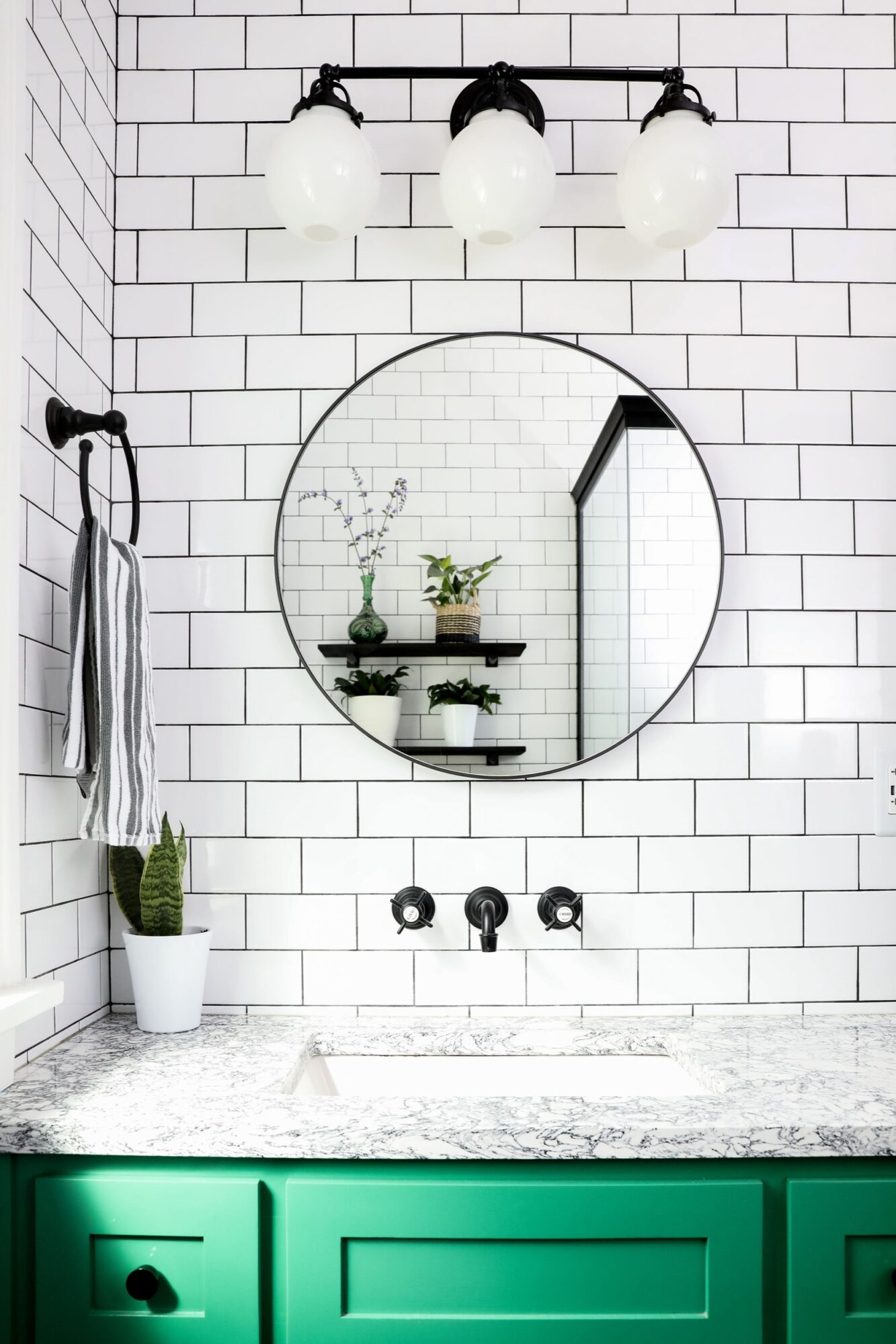 Seattle's best commercial food and hospitality photographer A modern bathroom with white subway tile walls, a round mirror, black fixtures, a green vanity with a marble countertop, a small potted plant, and striped towel hanging on the wall—styled like Seattles best commercial food lifestyle photographer would capture. captured by seattle's best food and lifestyle photographer Brooke Fitts