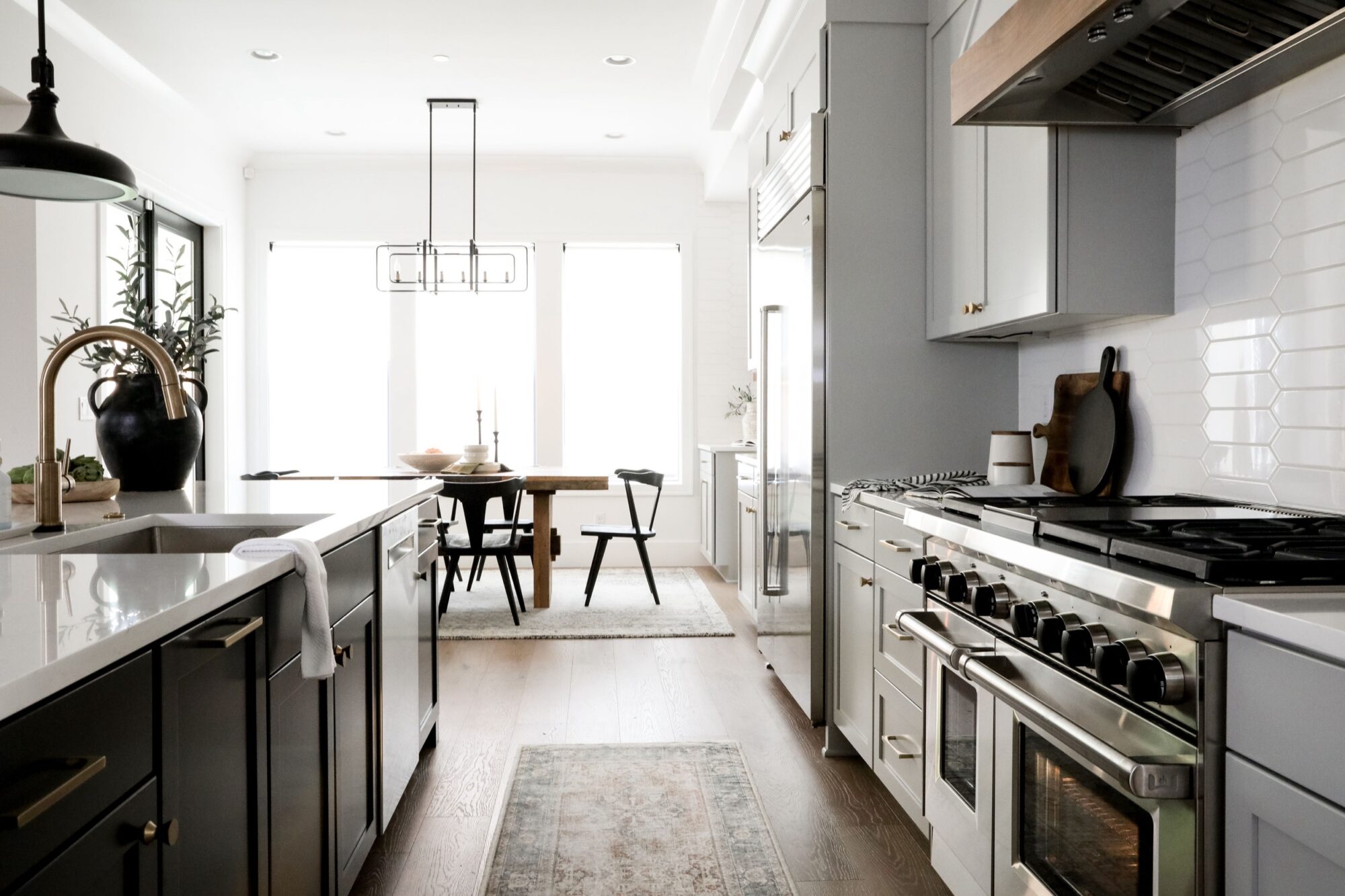 Seattle's best commercial food and hospitality photographer Modern kitchen with white cabinets, stainless steel appliances, and a large island with a sink—captured by Seattles best commercial food lifestyle photographer. A wooden dining table with black chairs sits in the bright dining area at the far end. captured by seattle's best food and lifestyle photographer Brooke Fitts