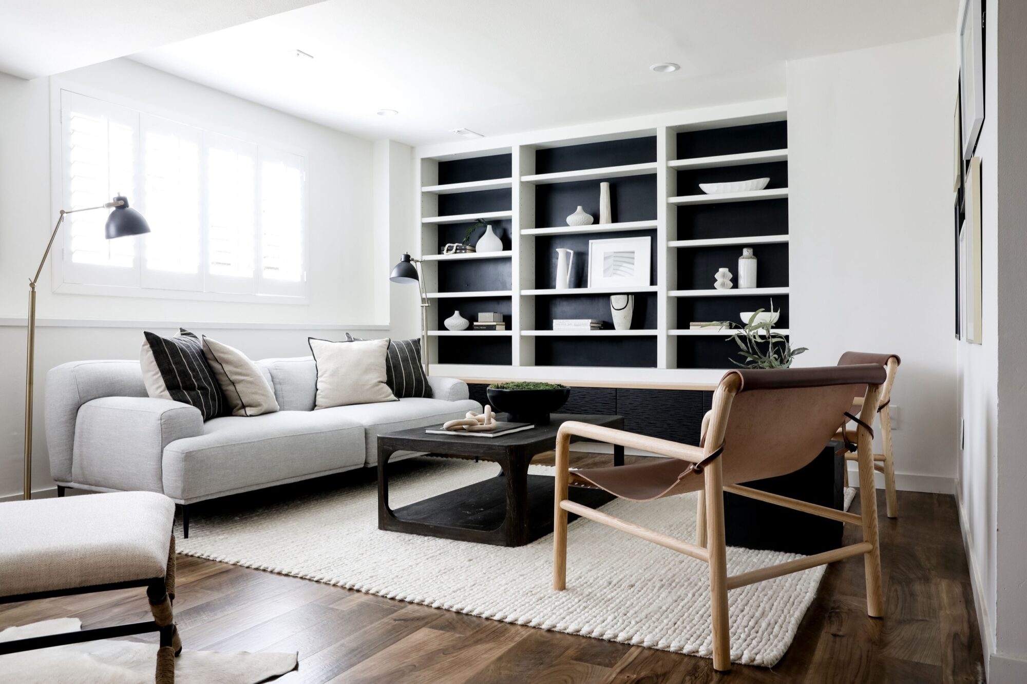 Seattle's best commercial food and hospitality photographer A modern living room with a light gray sofa, tan leather chairs, a black coffee table, a white textured rug, hardwood floors, and a large built-in bookshelf—styled by Seattles best commercial food lifestyle photographer. captured by seattle's best food and lifestyle photographer Brooke Fitts