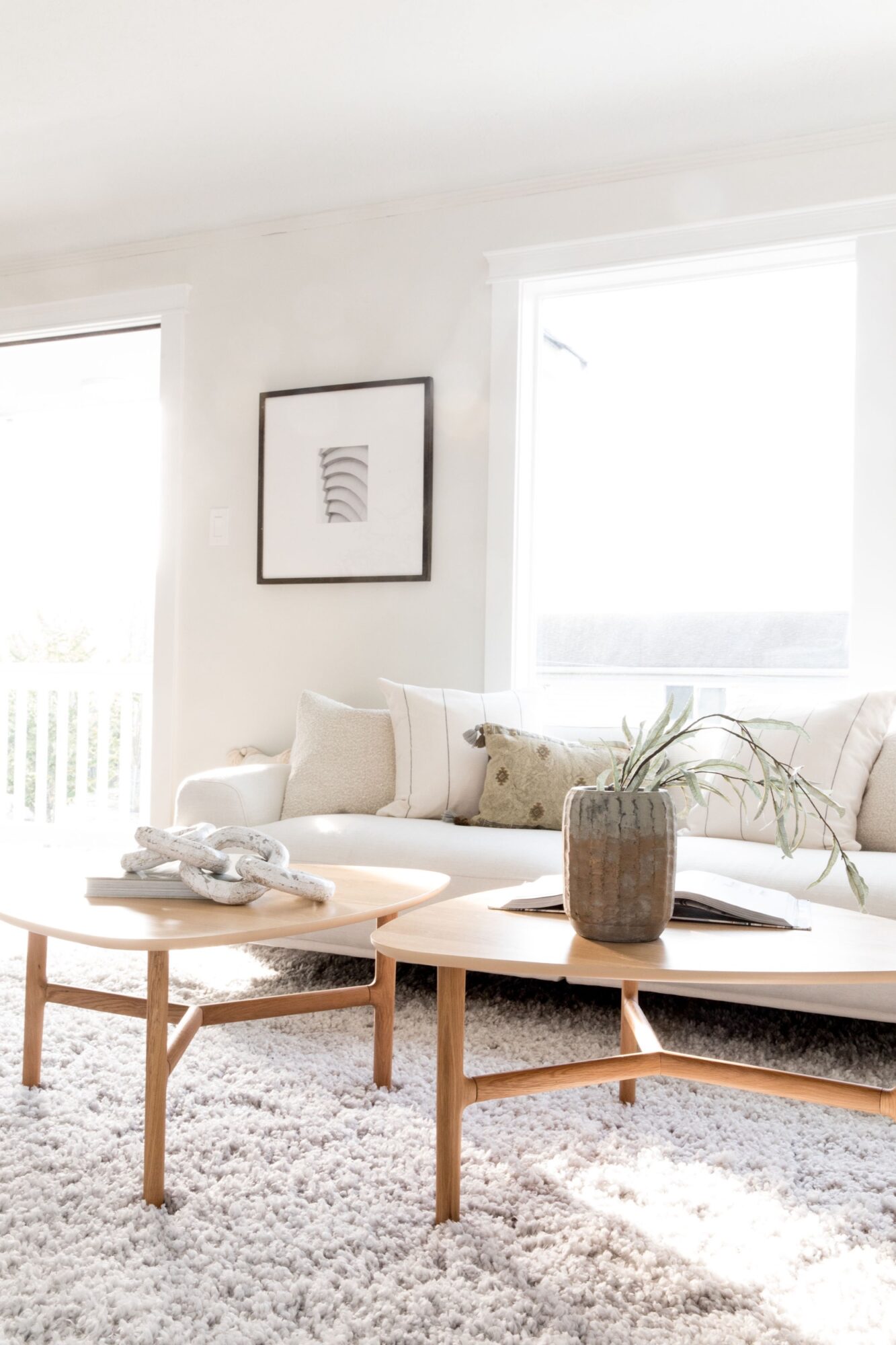 Seattle's best commercial food and hospitality photographer A bright, minimalist living room with a white couch, neutral pillows, light wood coffee tables, and framed abstract art on the wall—captured in the style of Seattles best commercial food lifestyle photographer. Sunlight streams through large windows. captured by seattle's best food and lifestyle photographer Brooke Fitts