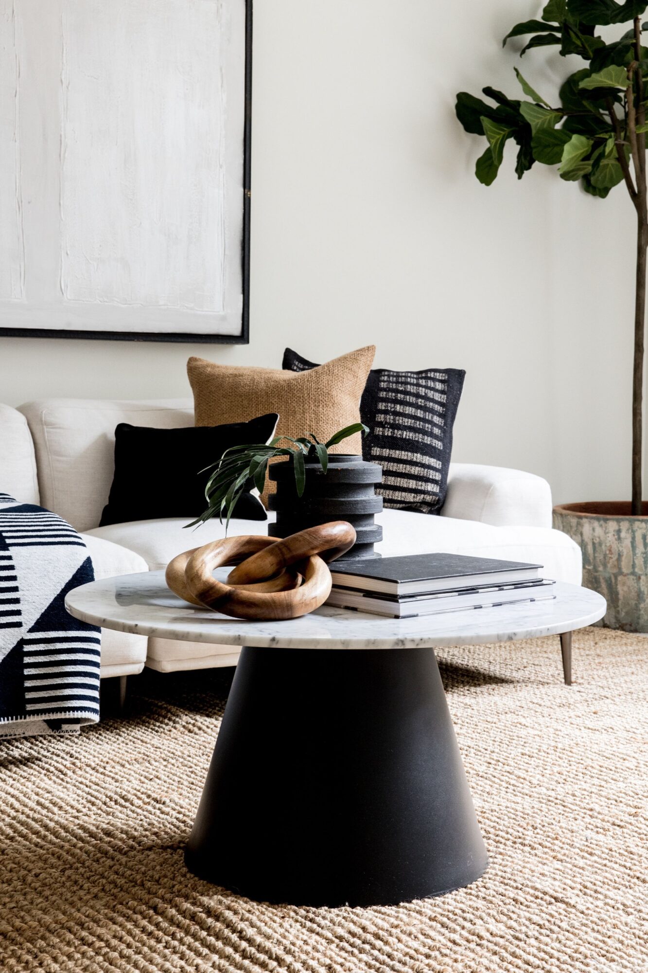 Seattle's best commercial food and hospitality photographer A modern living room styled by Seattles best commercial food lifestyle photographer, featuring a round marble coffee table with stacked books, wooden decor rings, and a small plant. Behind it sits a white sofa with patterned pillows and a potted plant in the corner. captured by seattle's best food and lifestyle photographer Brooke Fitts