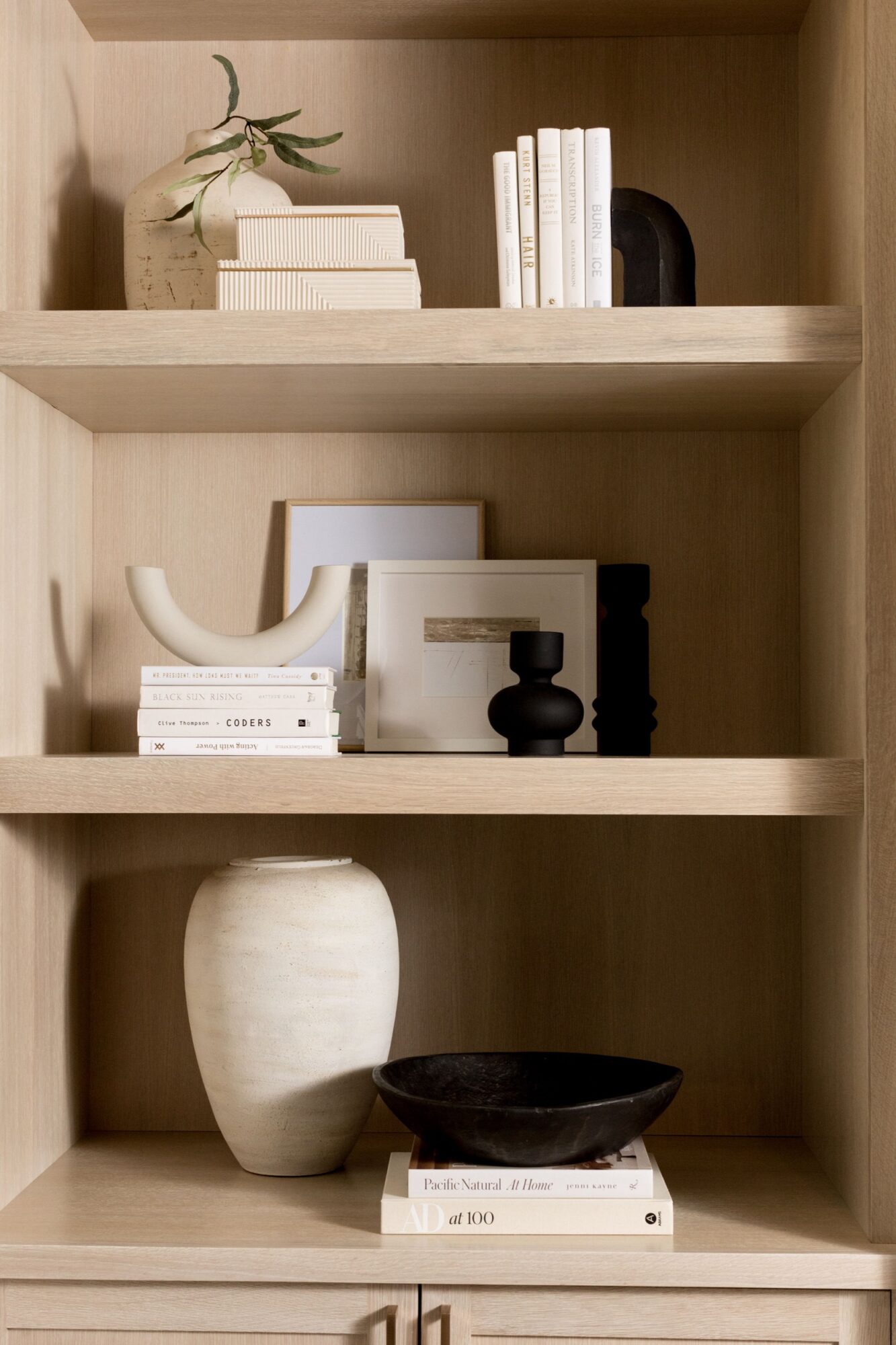Seattle's best commercial food and hospitality photographer Three wooden shelves display white and black ceramic vases, stacked books, a small plant, and framed art in a minimalist, neutral-toned arrangement styled by Seattles best commercial food lifestyle photographer. captured by seattle's best food and lifestyle photographer Brooke Fitts