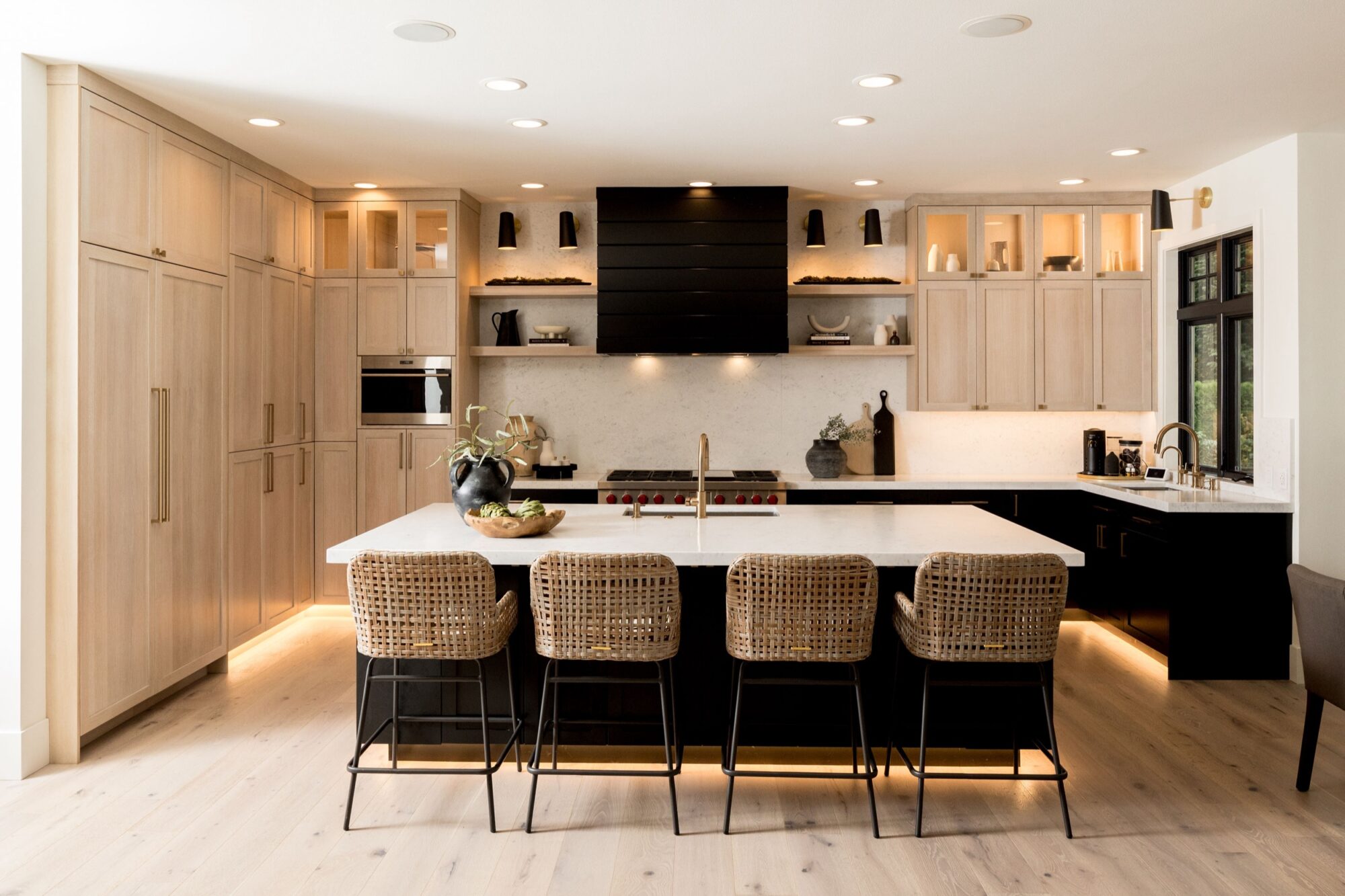 Seattle's best commercial food and hospitality photographer Modern kitchen with light wood cabinets, a large island with marble countertop, four woven barstools, black accents, built-in appliances, and decorative shelves—styled by Seattles best commercial food lifestyle photographer. captured by seattle's best food and lifestyle photographer Brooke Fitts