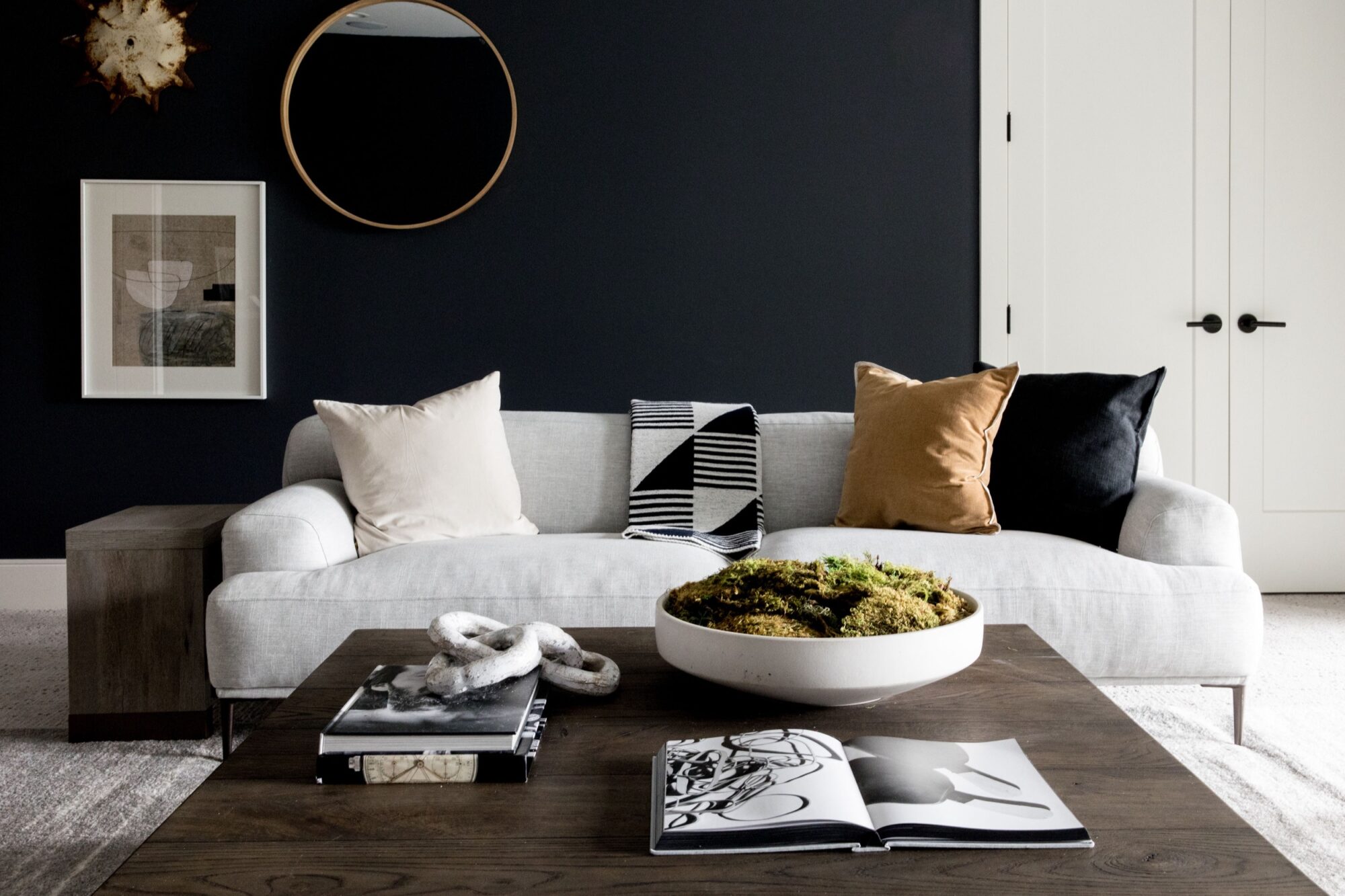 Seattle's best commercial food and hospitality photographer A modern living room with a gray couch, three pillows, a striped throw, dark accent wall, framed art, round mirror, and wooden coffee table styled by Seattles best commercial food lifestyle photographer. captured by seattle's best food and lifestyle photographer Brooke Fitts