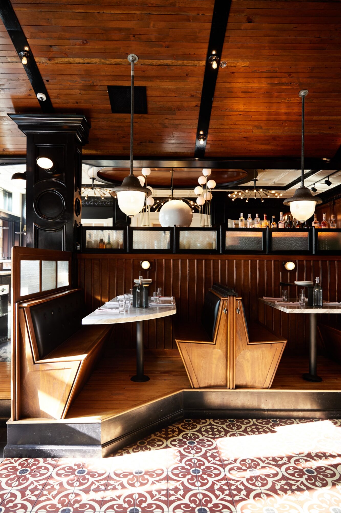 Seattle's best commercial food and hospitality photographer A stylish restaurant interior with wooden booths, marble tables, globe pendant lights, and patterned tile flooring—captured by Seattles best commercial food lifestyle photographer. Sunlight streams in, highlighting the warm wood ceiling and modern decor. captured by seattle's best food and lifestyle photographer Brooke Fitts