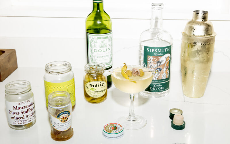 Seattle's best commercial food and hospitality photographer A martini garnished with a lemon twist sits on a white counter, surrounded by an open gin bottle, vermouth, and cocktail essentials—artfully styled by Seattles best commercial food lifestyle photographer. captured by seattle's best food and lifestyle photographer Brooke Fitts