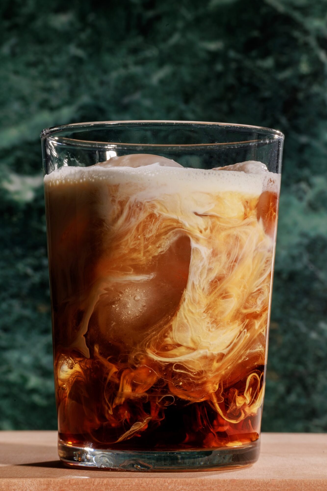 Seattle's best commercial food and hospitality photographer A glass of iced coffee with swirling cream sits on a wooden surface in front of a dark green marble background, captured by Seattles best commercial food lifestyle photographer. captured by seattle's best food and lifestyle photographer Brooke Fitts