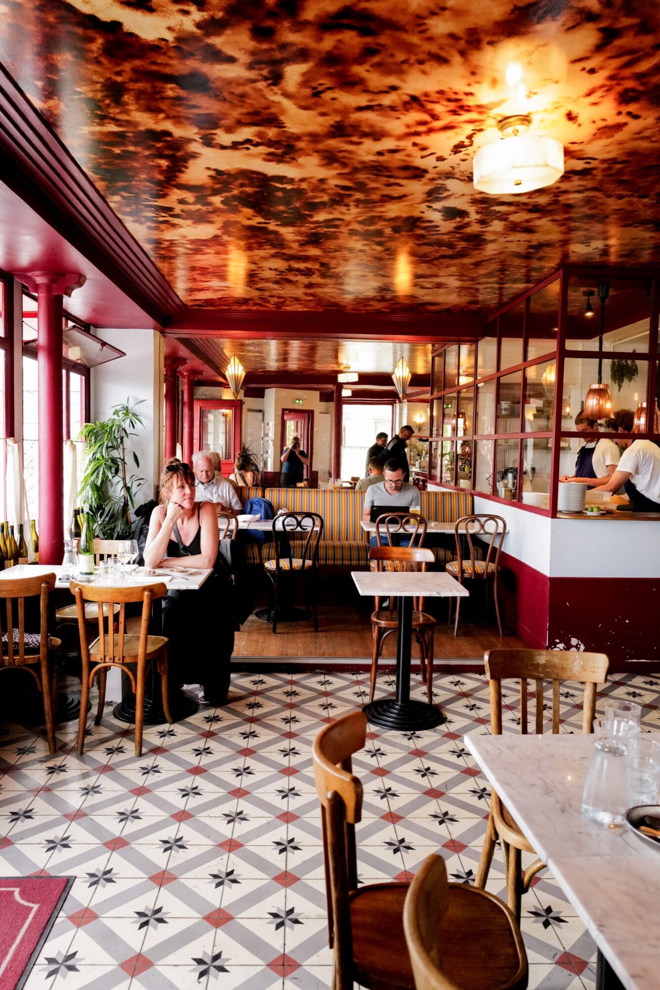 Seattle's best commercial food and hospitality photographer A cozy café with patterned tile floors, wooden chairs, and marble tables—captured perfectly by Seattles best commercial food lifestyle photographer. People chat or work behind a glass partition beneath a dramatic, cloud-like ceiling in warm tones. captured by seattle's best food and lifestyle photographer Brooke Fitts