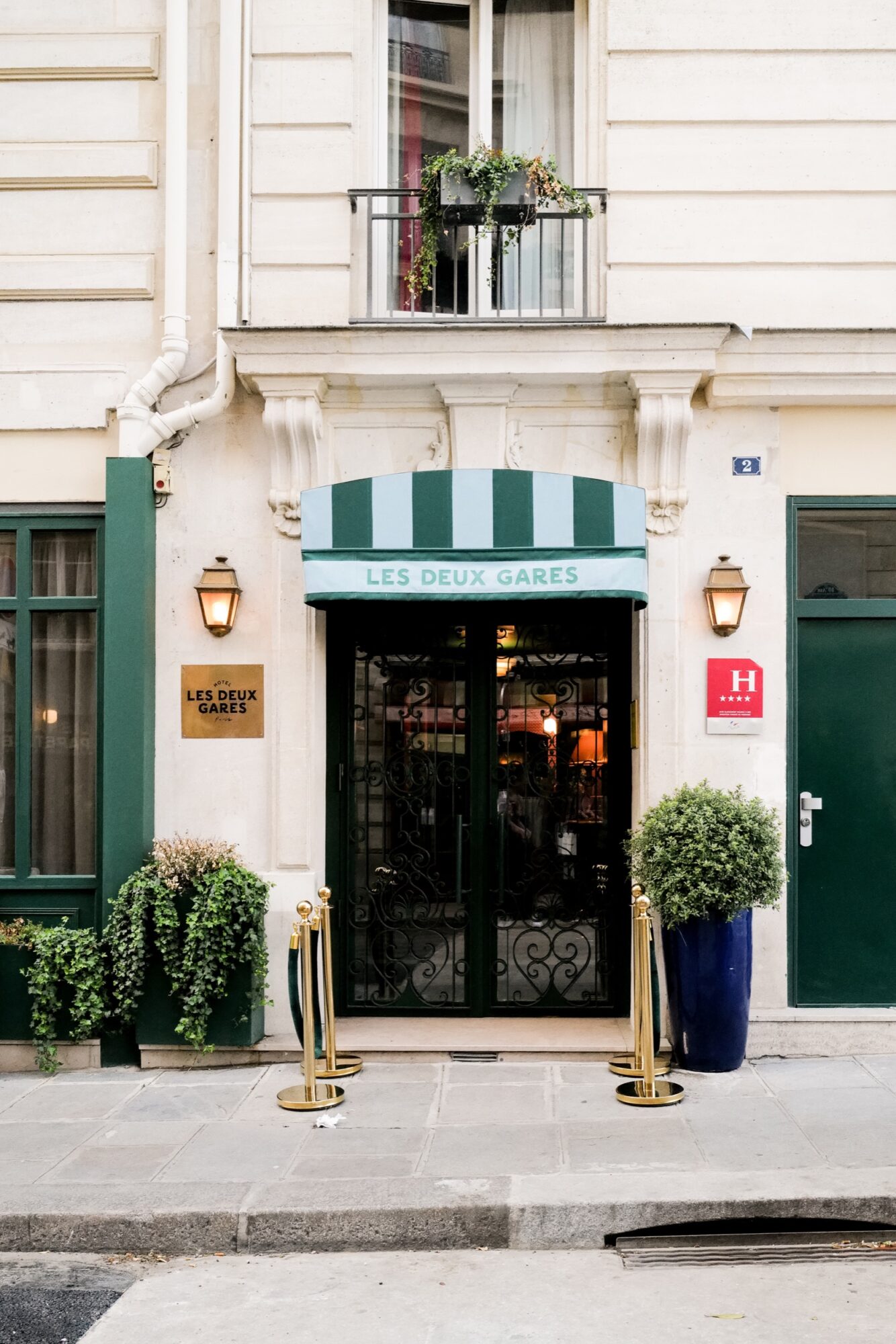 Seattle's best commercial food and hospitality photographer Entrance of Les Deux Gares hotel with green-striped awning, potted plants, brass poles and ropes—captured with the eye of Seattle’s best commercial food lifestyle photographer—plus wall lamps and a flower-adorned balcony above the light facade. captured by seattle's best food and lifestyle photographer Brooke Fitts