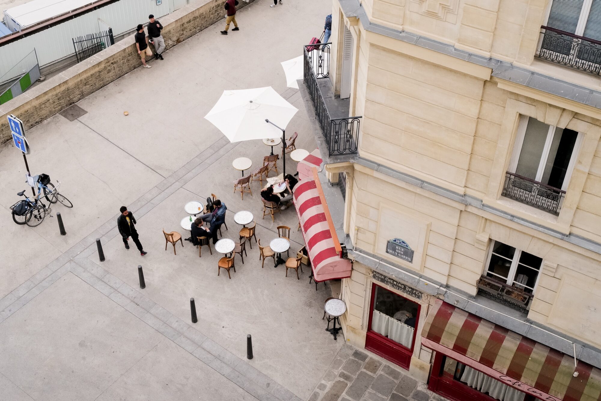 Seattle's best commercial food and hospitality photographer Aerial view by Seattles best commercial food lifestyle photographer: a small outdoor café with empty tables, a few people relaxing under a white umbrella, and red-striped awnings lining a quiet city street. captured by seattle's best food and lifestyle photographer Brooke Fitts