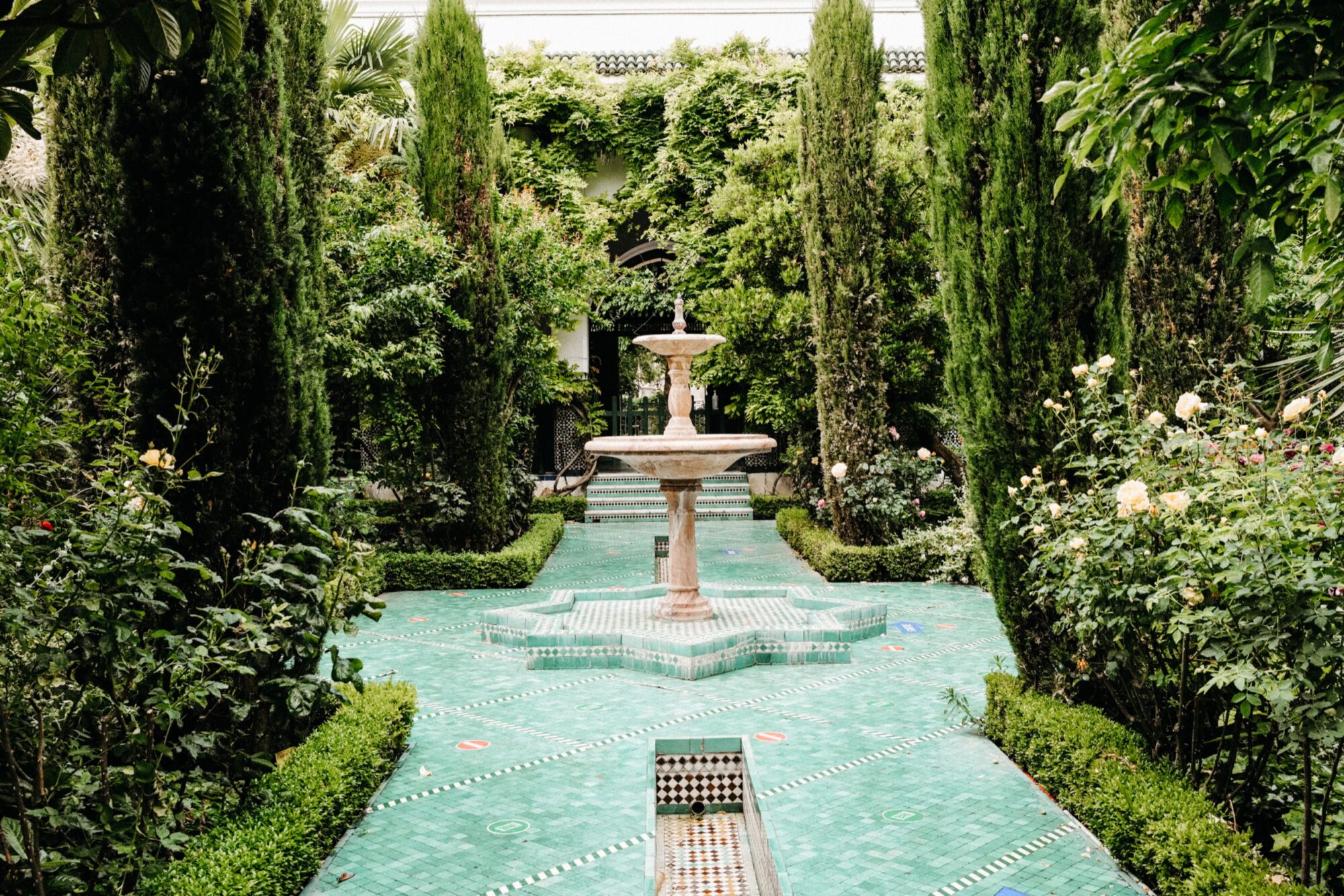 Seattle's best commercial food and hospitality photographer A lush garden with tall green trees, manicured hedges, and flowering bushes surrounds a central tiled fountain on a decorative green mosaic pathway—captured by Seattles best commercial food lifestyle photographer. captured by seattle's best food and lifestyle photographer Brooke Fitts