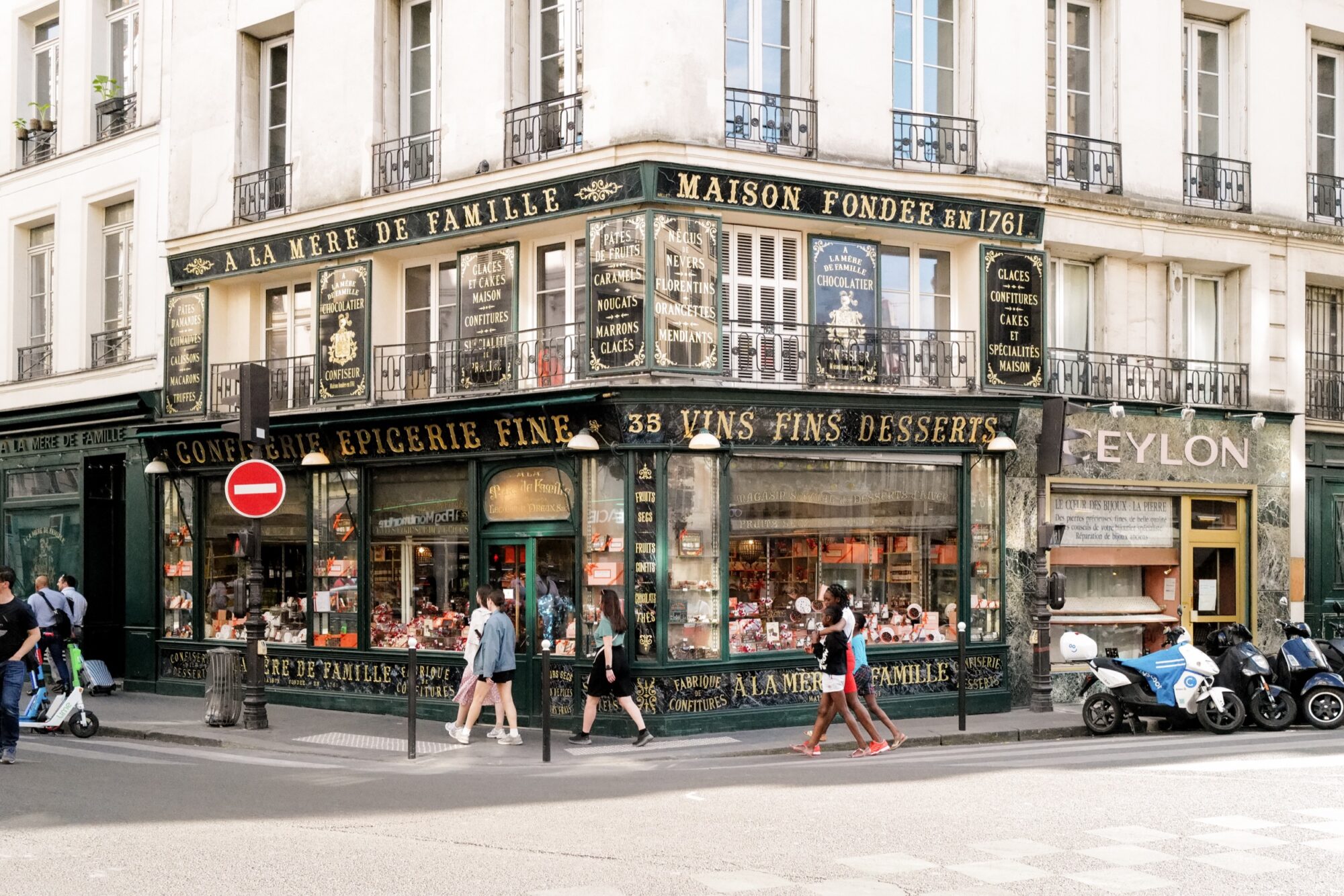 Seattle's best commercial food and hospitality photographer Corner view of a vintage French shop, A La Mère de Famille, with green and gold signage, large windows displaying sweets, and people walking by—captured in the style of Seattles best commercial food lifestyle photographer. Scooters line the street. captured by seattle's best food and lifestyle photographer Brooke Fitts