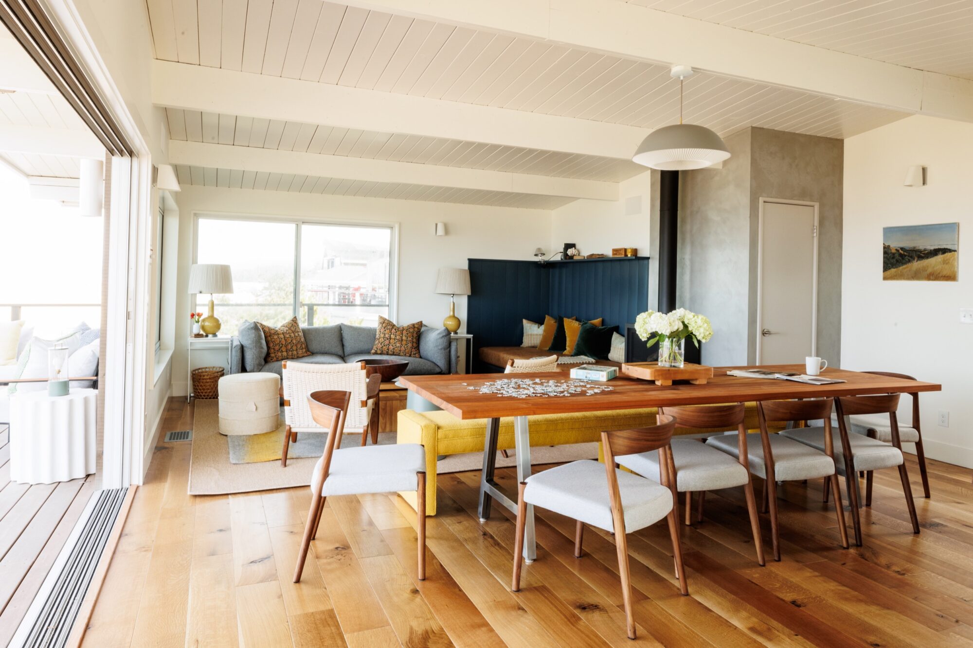 Seattle's best commercial food and hospitality photographer Open-concept living and dining area with wood floors, a wooden dining table for six, cozy gray sectional sofa, cushions, and large windows filling the space with natural light—captured by a Seattle commercial interior design photographer. captured by seattle's best food and lifestyle photographer Brooke Fitts